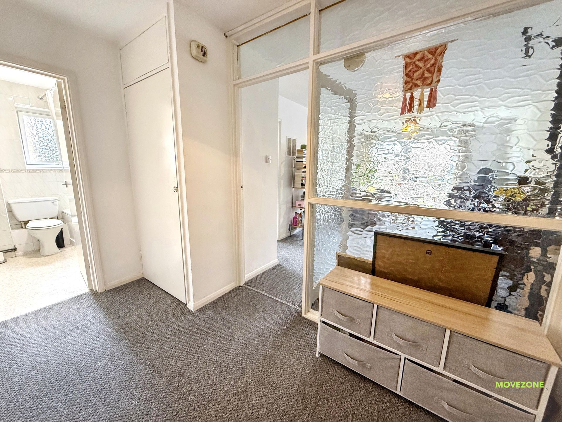 Bright hallway with frosted glass door, carpet, white walls, and small cabinet by an entryway.