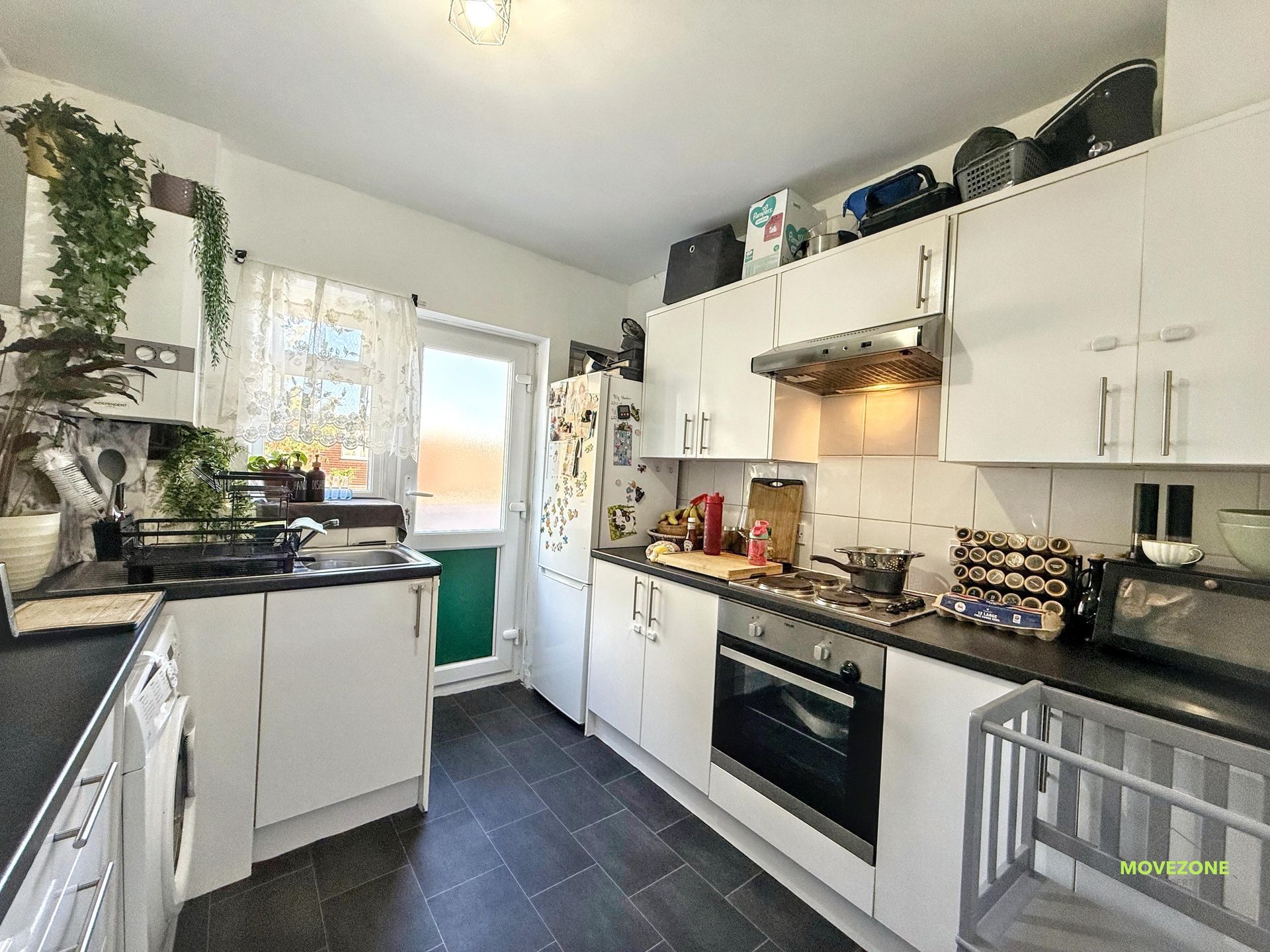 Bright white kitchen with black countertops, stainless oven, tiled floor, and a sunlit back door