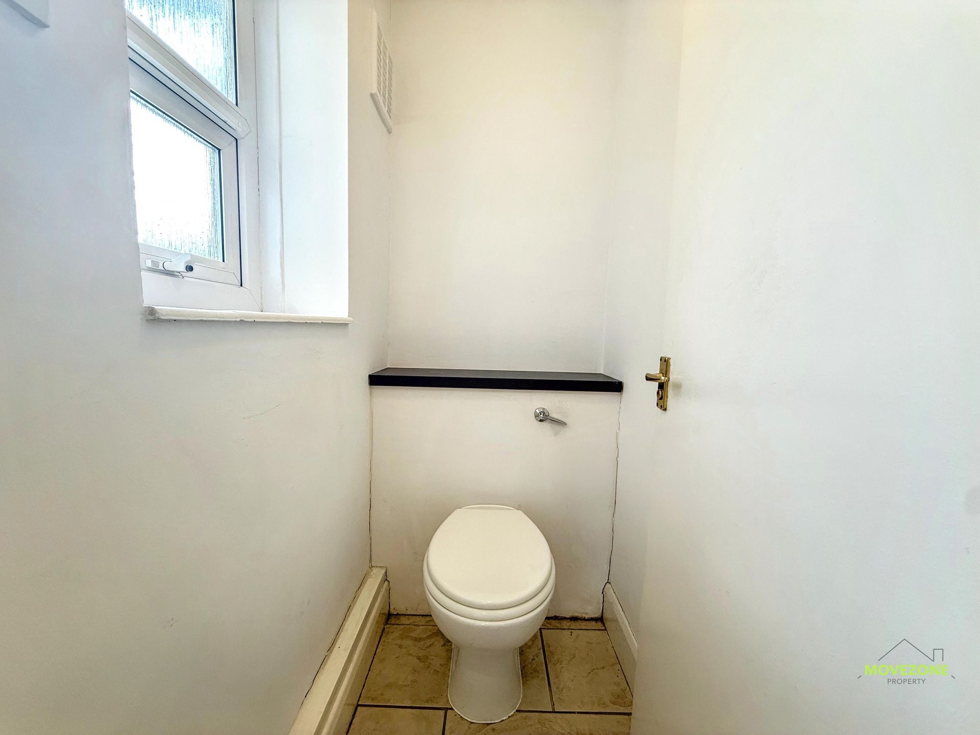 Small white bathroom with a toilet, window, grab bar, and beige tiled floor.