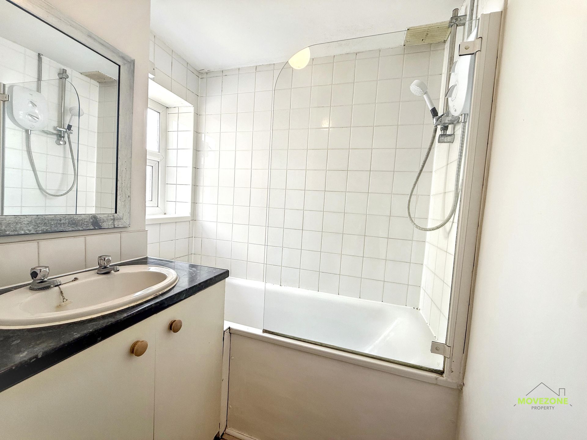 Small bathroom with a sink, mirror, and white tiled bathtub shower.