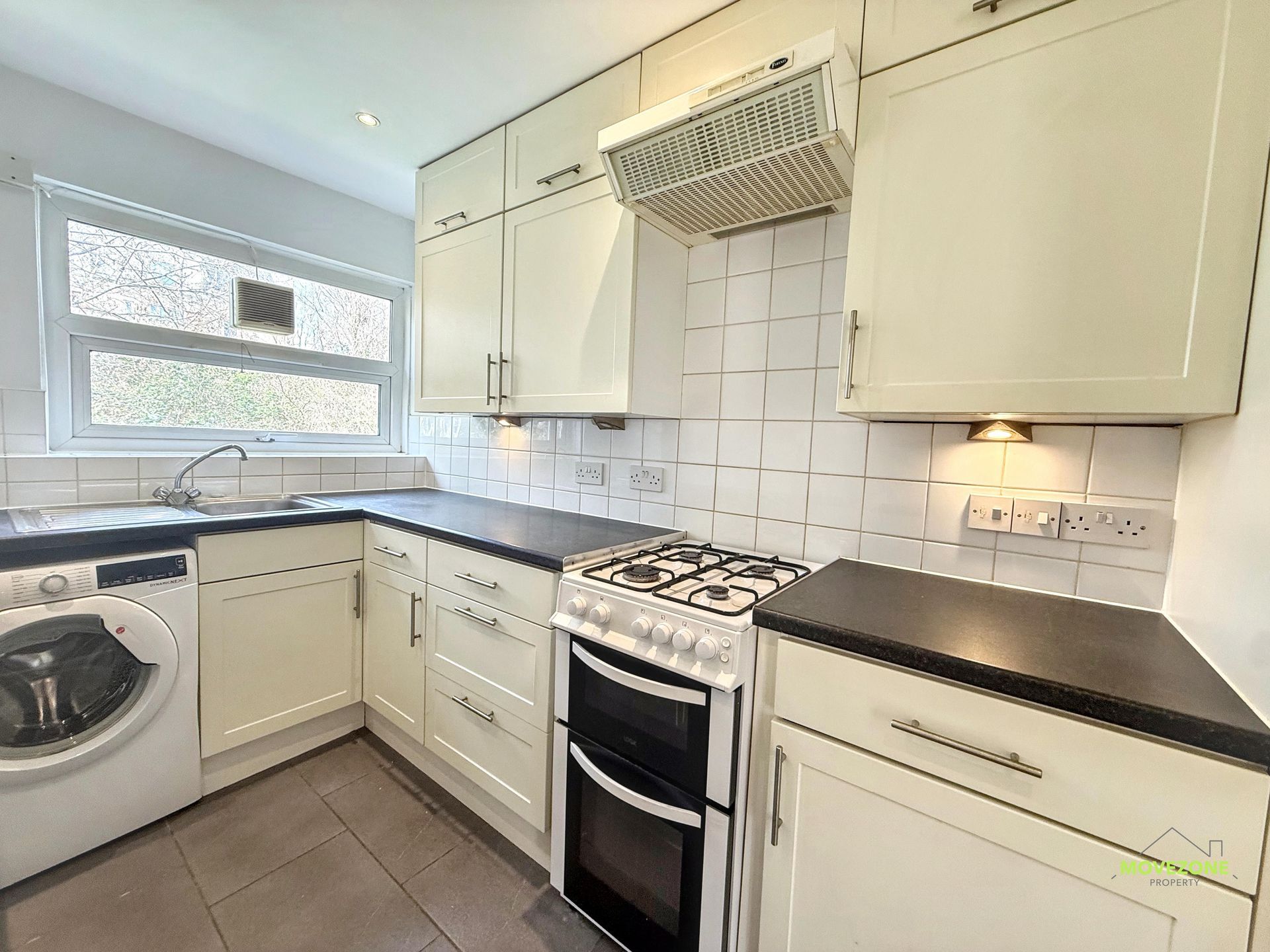 Bright modern kitchen with white cabinets, black countertops, gas stove, washing machine, and large window.