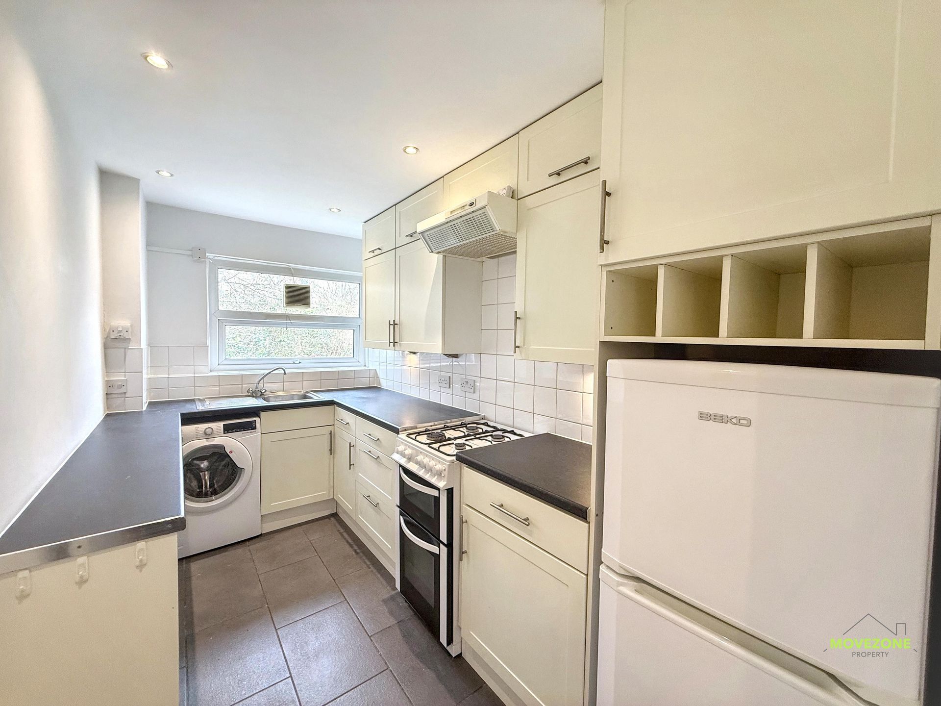 Compact white kitchen with black countertops, stove, washing machine, and bright window at the end