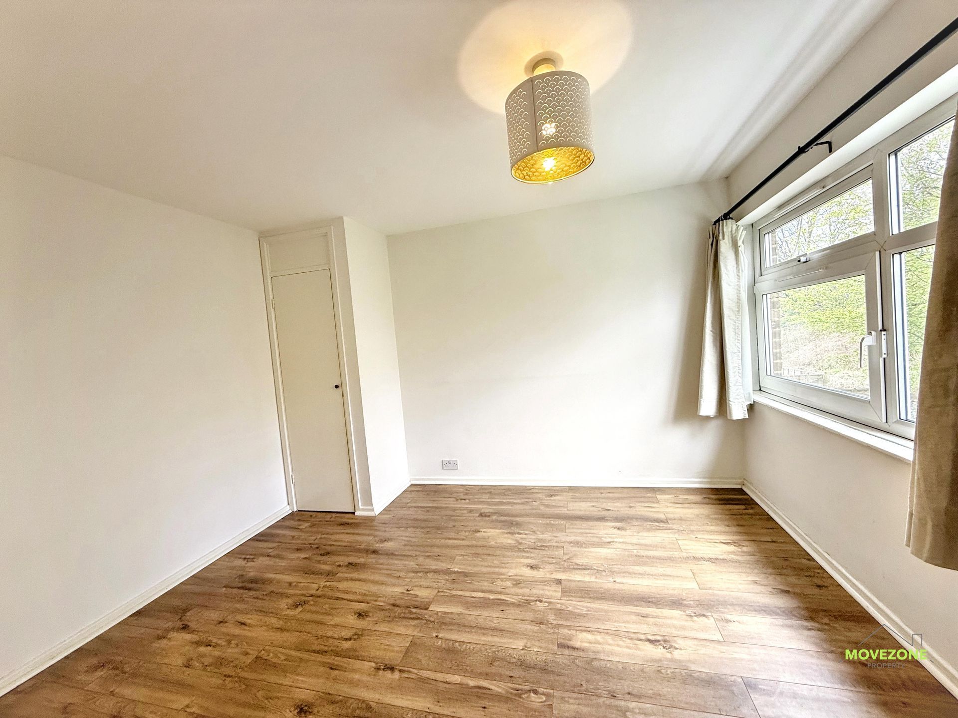 Empty white bedroom with wood flooring, a built-in closet, and a large window with curtains