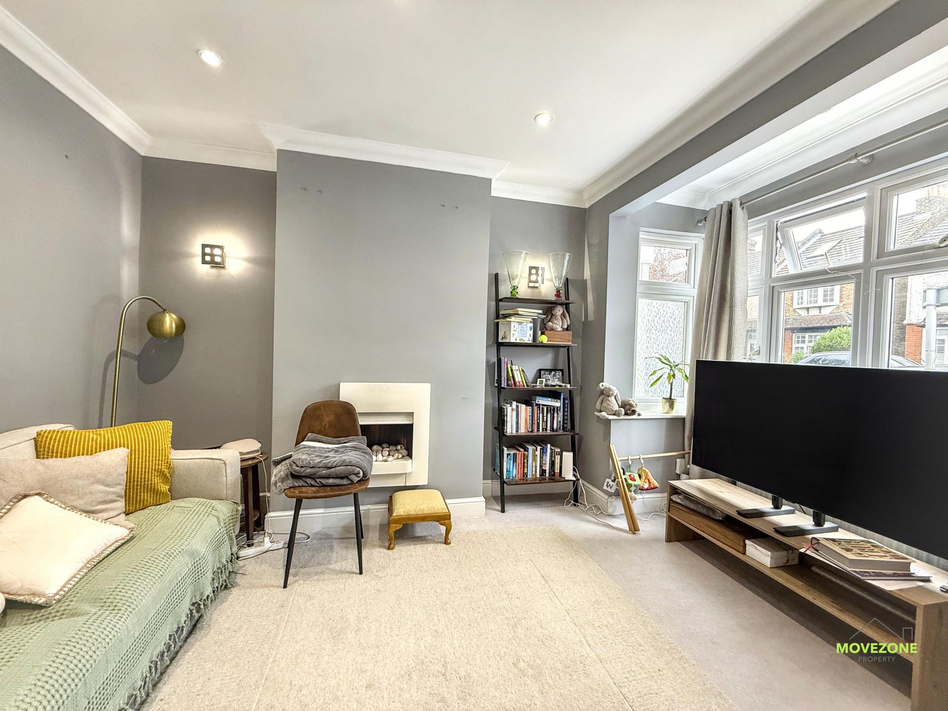 Bright living room with gray walls, beige sofa, fireplace, large TV, and bookshelves near a window.