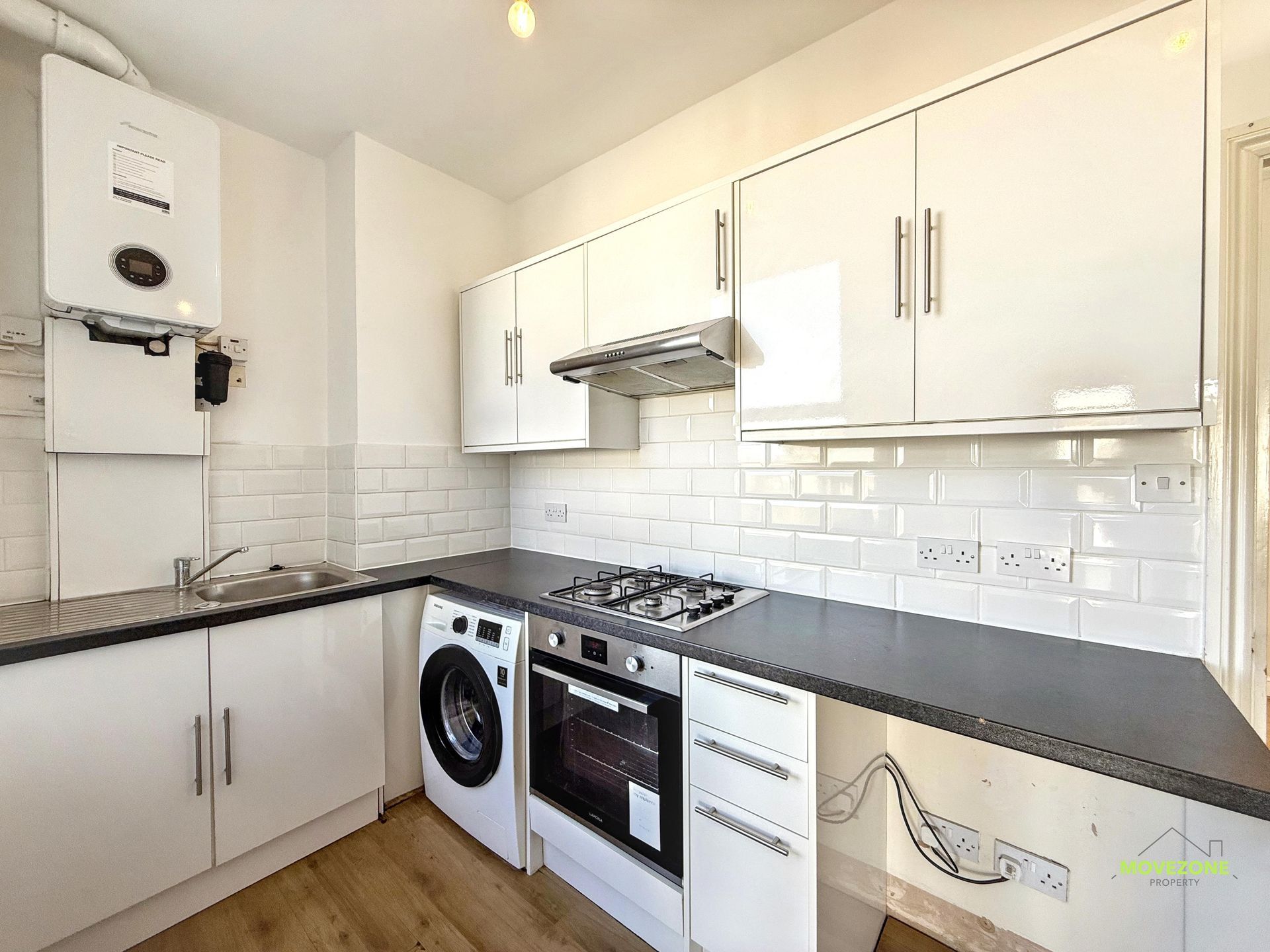 Modern white kitchen with black countertops, built-in oven, washing machine, and white subway tile backsplash