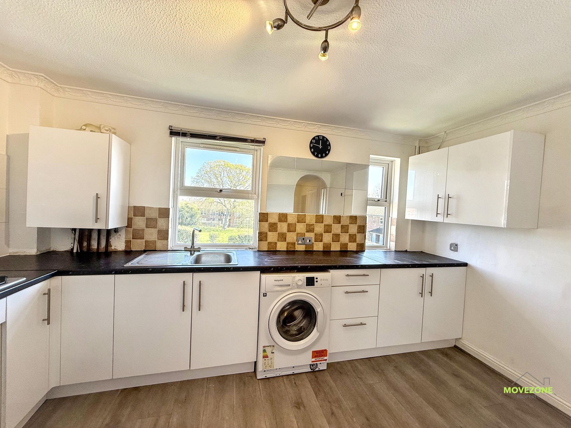 Bright white kitchen with black countertops, tiled backsplash, window, and a washing machine under the counter