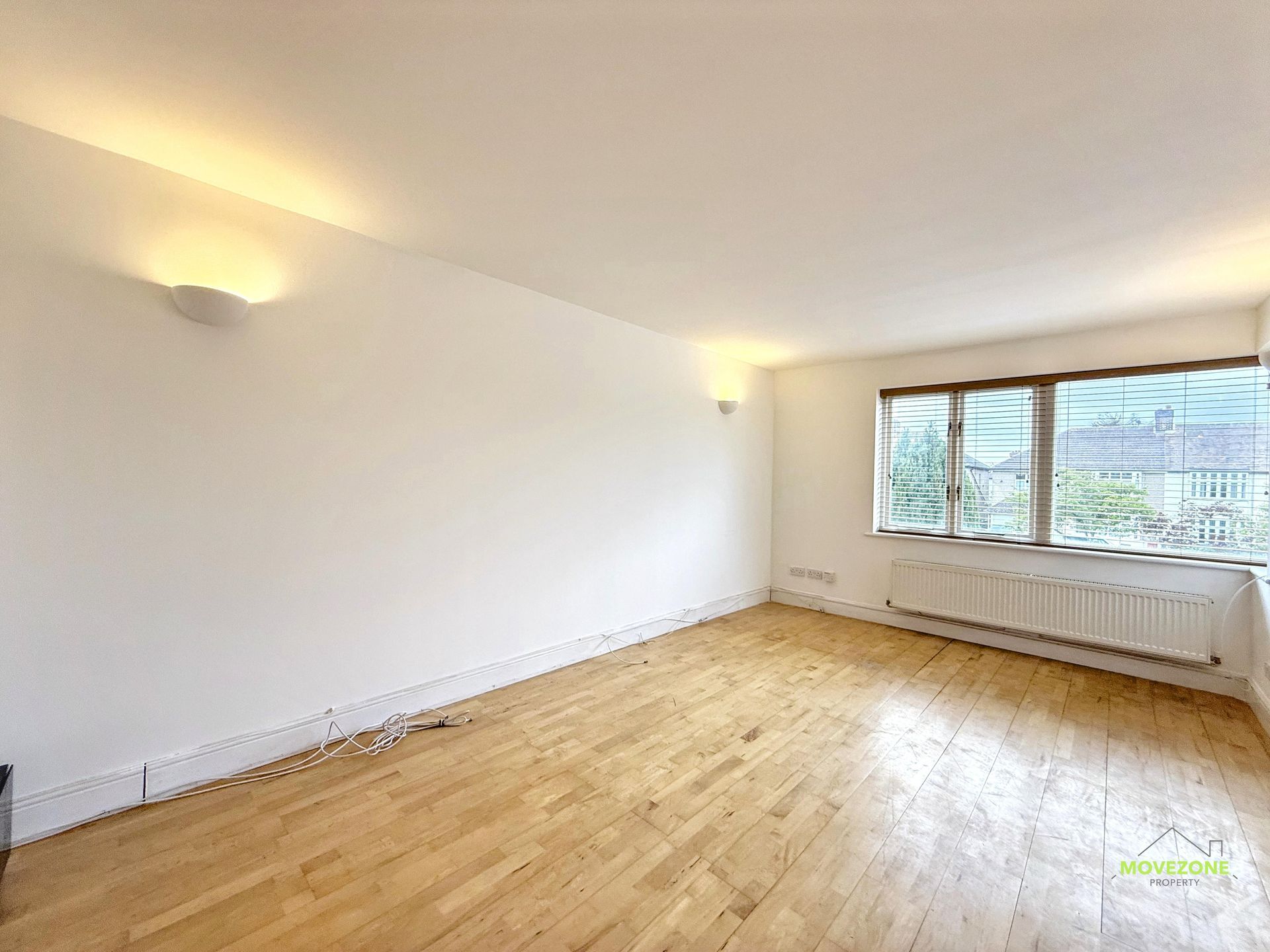 Empty white living room with wood floors and large window, lit by wall sconces