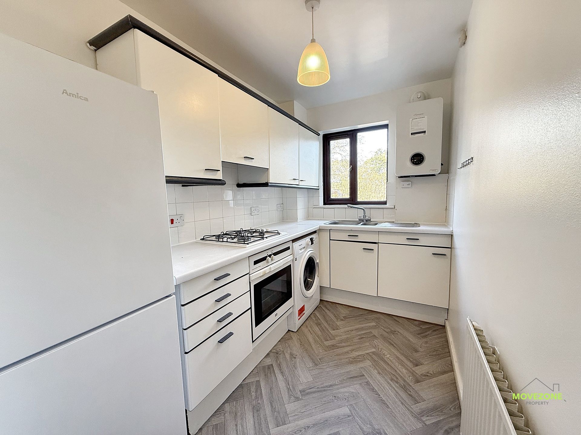 Modern white L-shaped kitchen with stove, oven, fridge, window, and herringbone floor