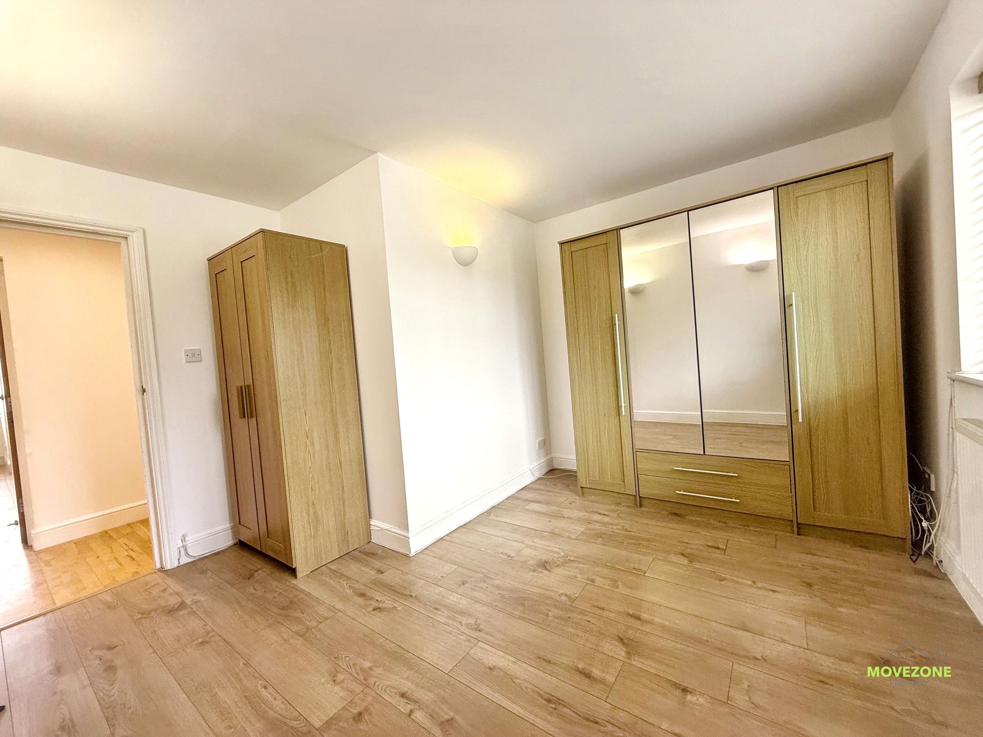 Empty bedroom with light wood floors, two wardrobes, and a mirrored closet.