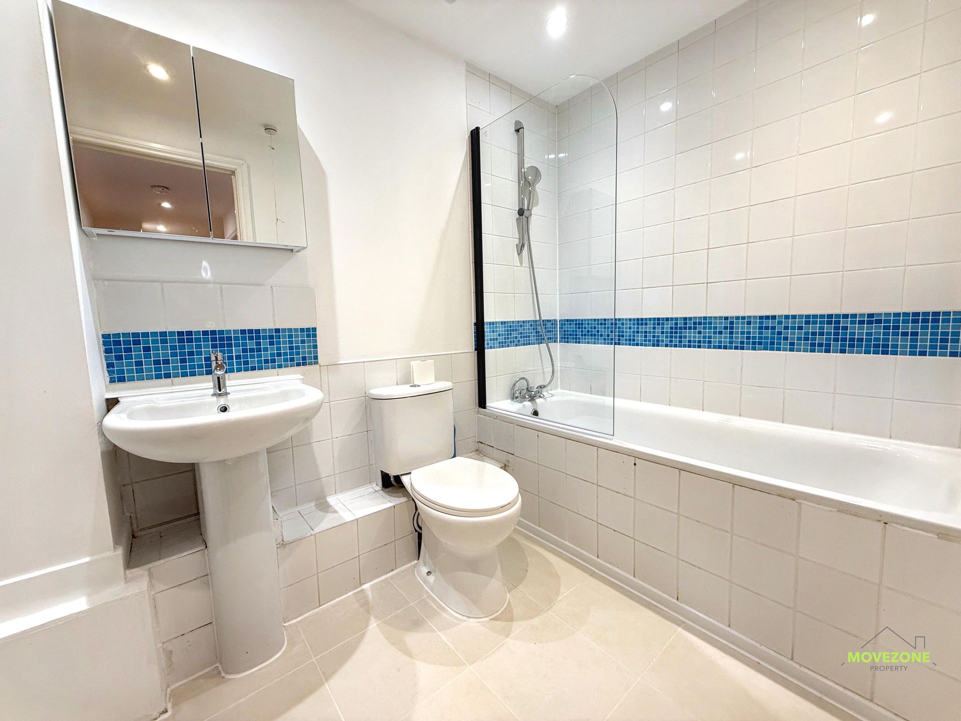 Bright white bathroom with sink, toilet, bathtub, and blue tile accent band