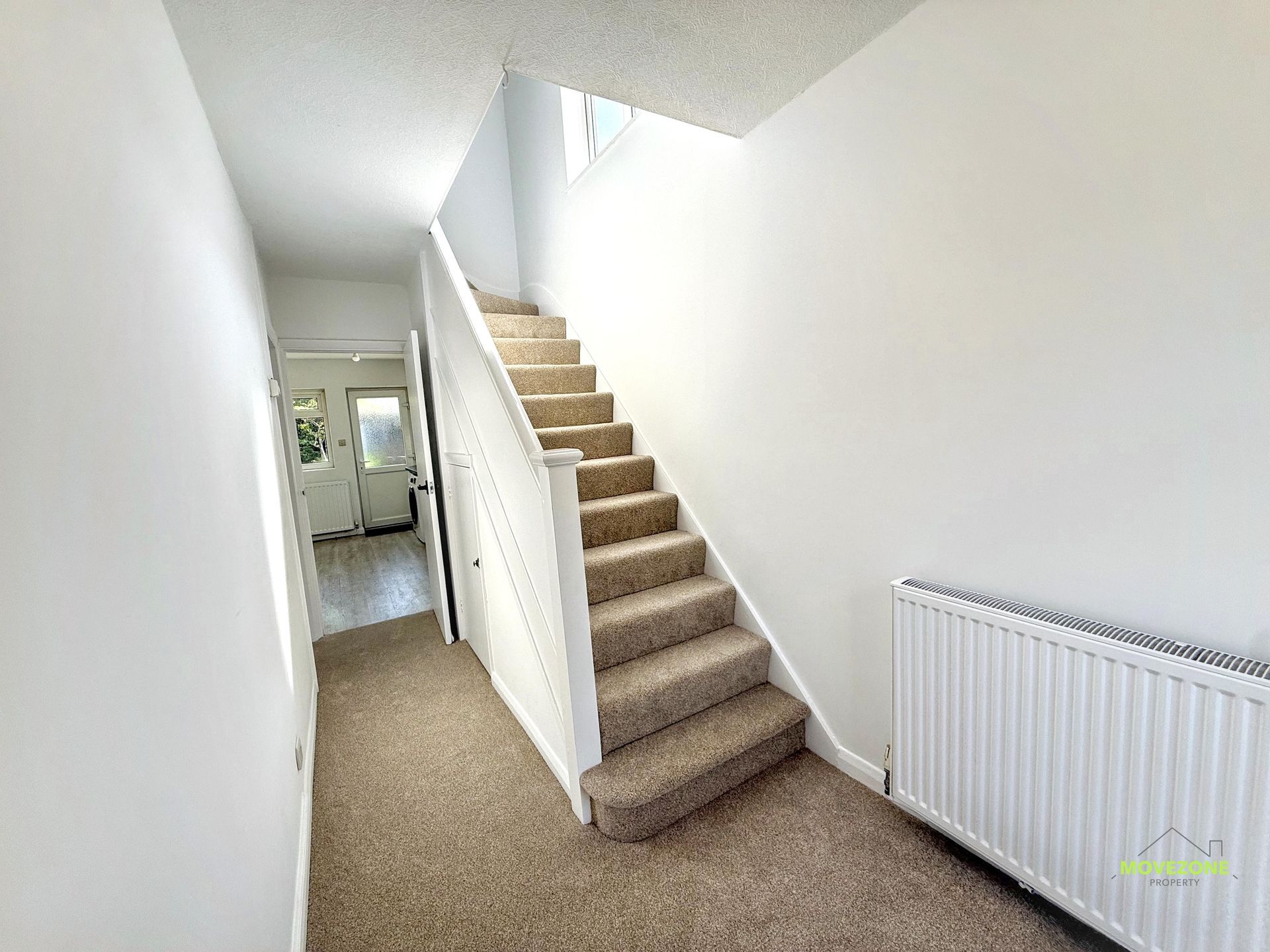 Bright hallway with carpeted stairs, white walls, skylight, and a radiator along the right wall.