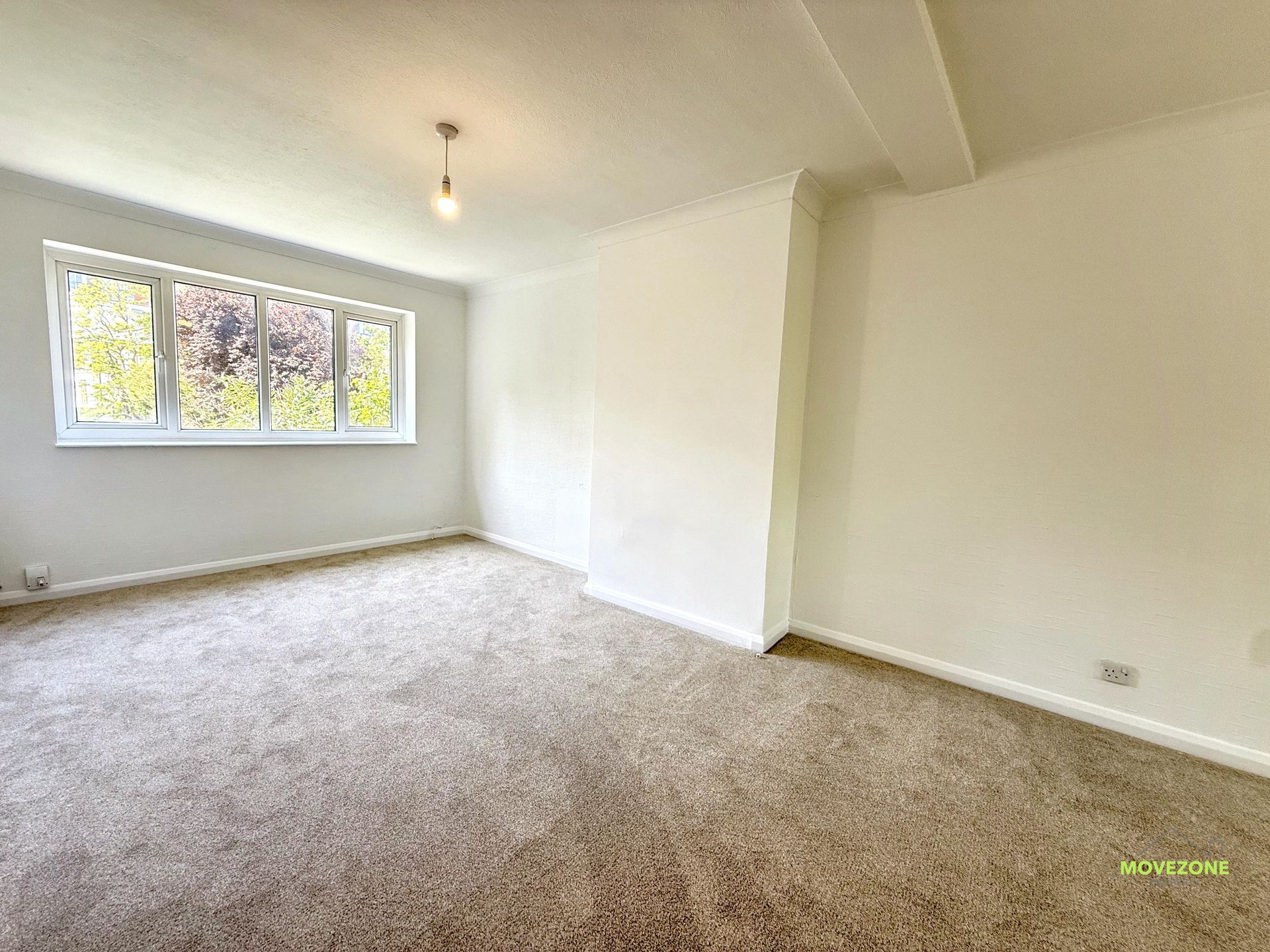 Empty carpeted bedroom with white walls and a window letting in natural light