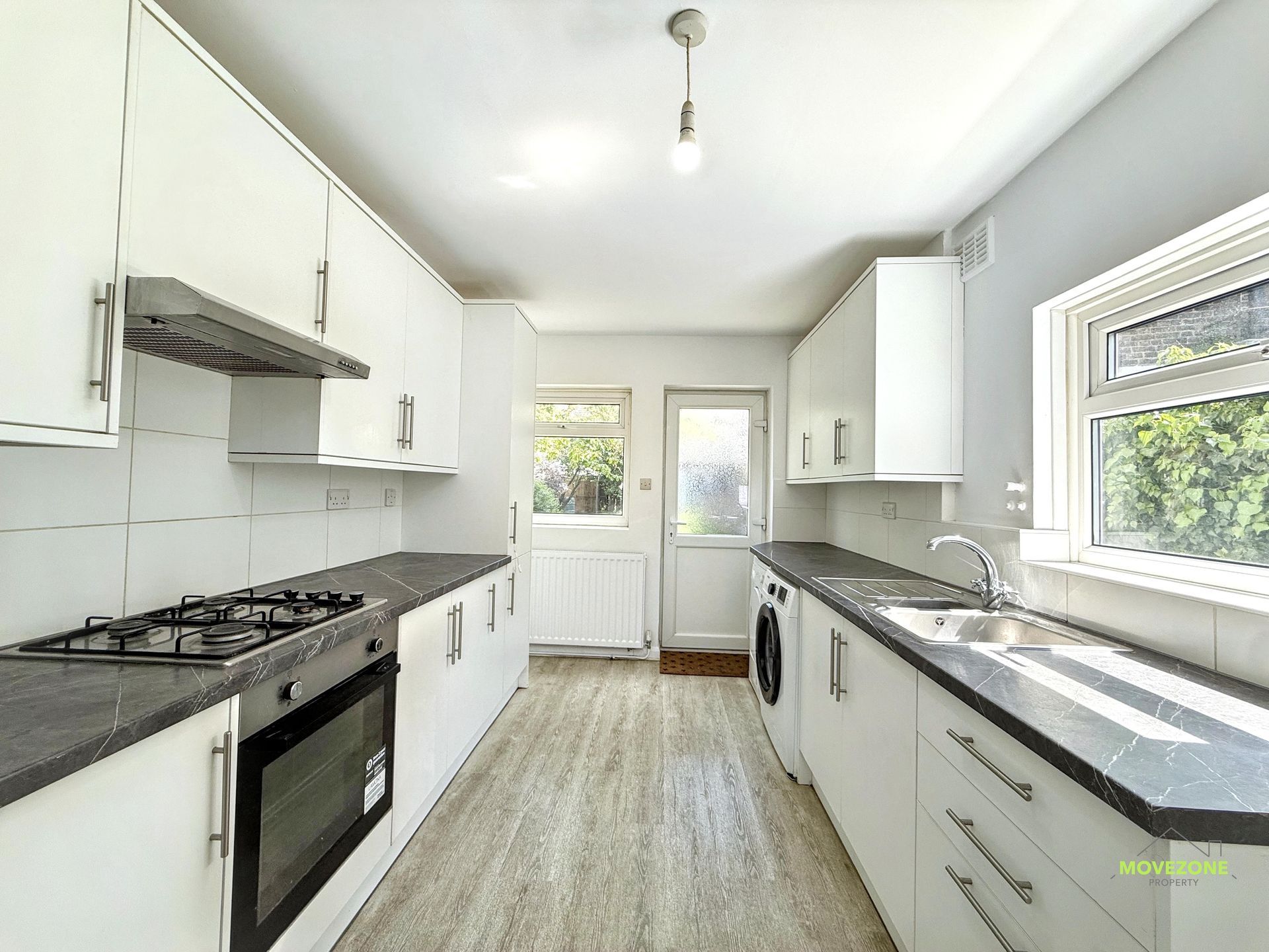Bright white galley kitchen with black stove, long countertops, and sunlight through windows