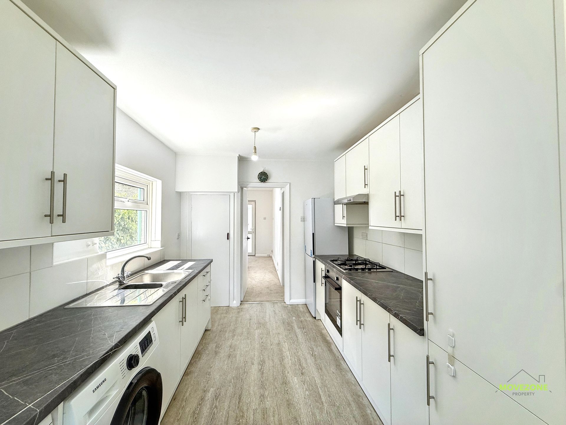 Bright modern galley kitchen with white cabinets, dark countertops, and wood-look flooring