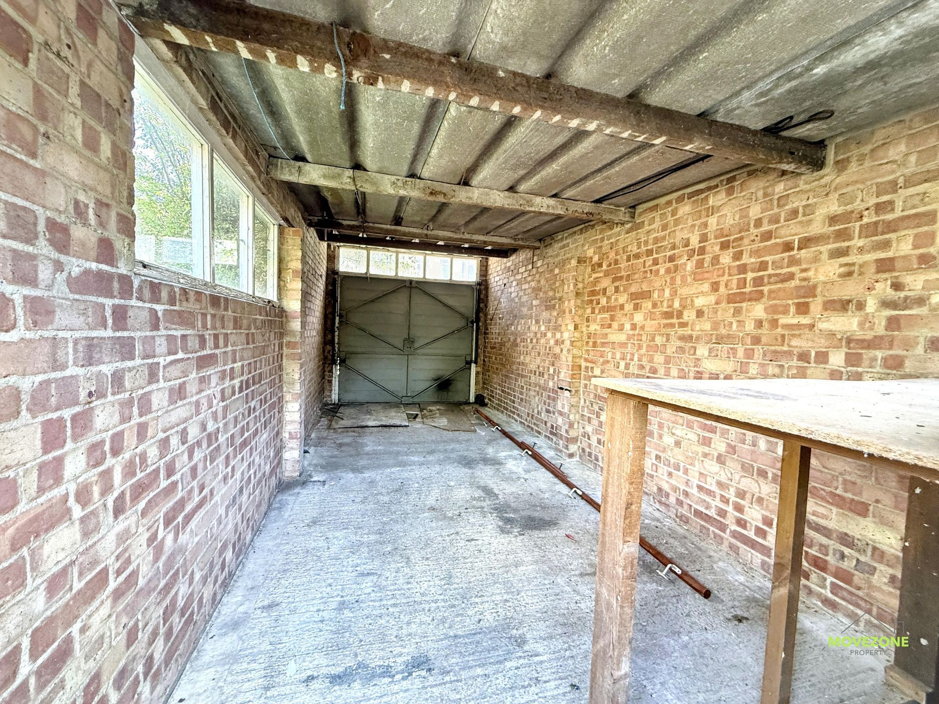 Narrow brick storage room with corrugated metal ceiling, concrete floor, and wooden table on the right.
