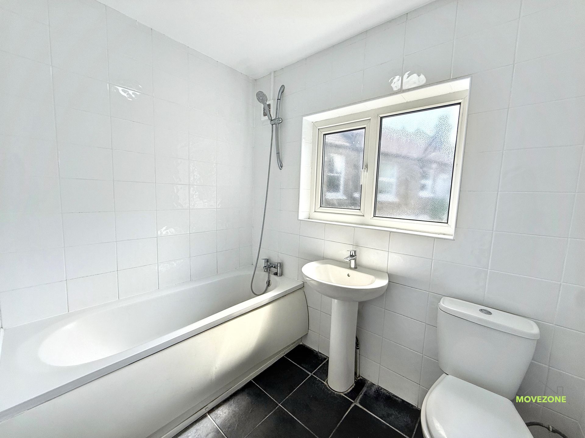 Bright white bathroom with bathtub, pedestal sink, mirror, and showerhead by the window.