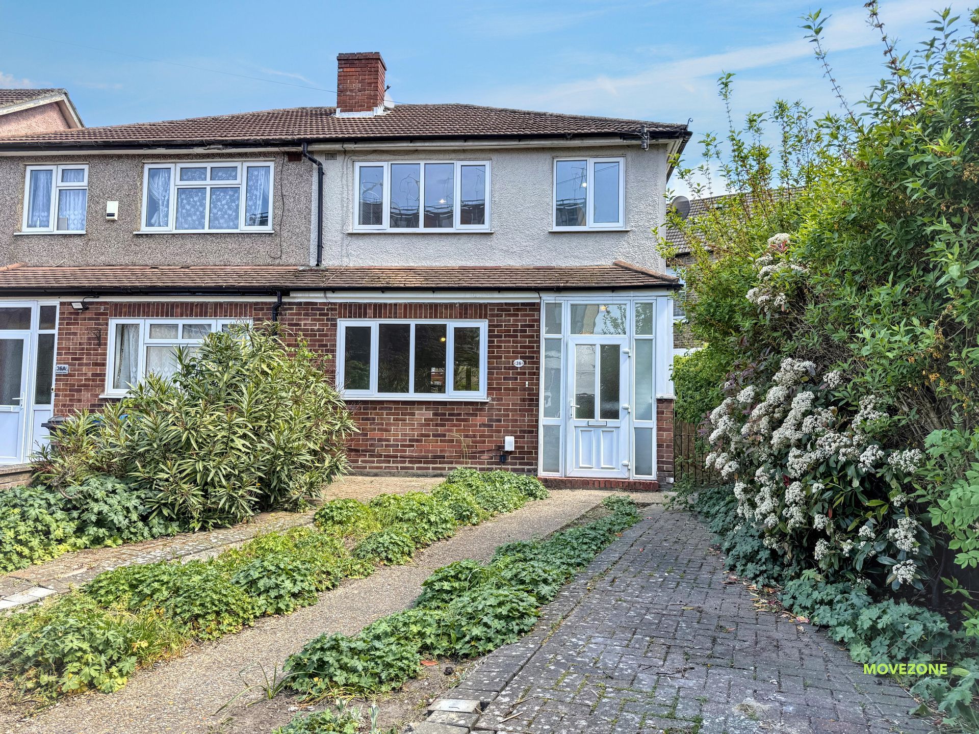 Semi-detached brick house with front garden and paved driveway under a blue sky