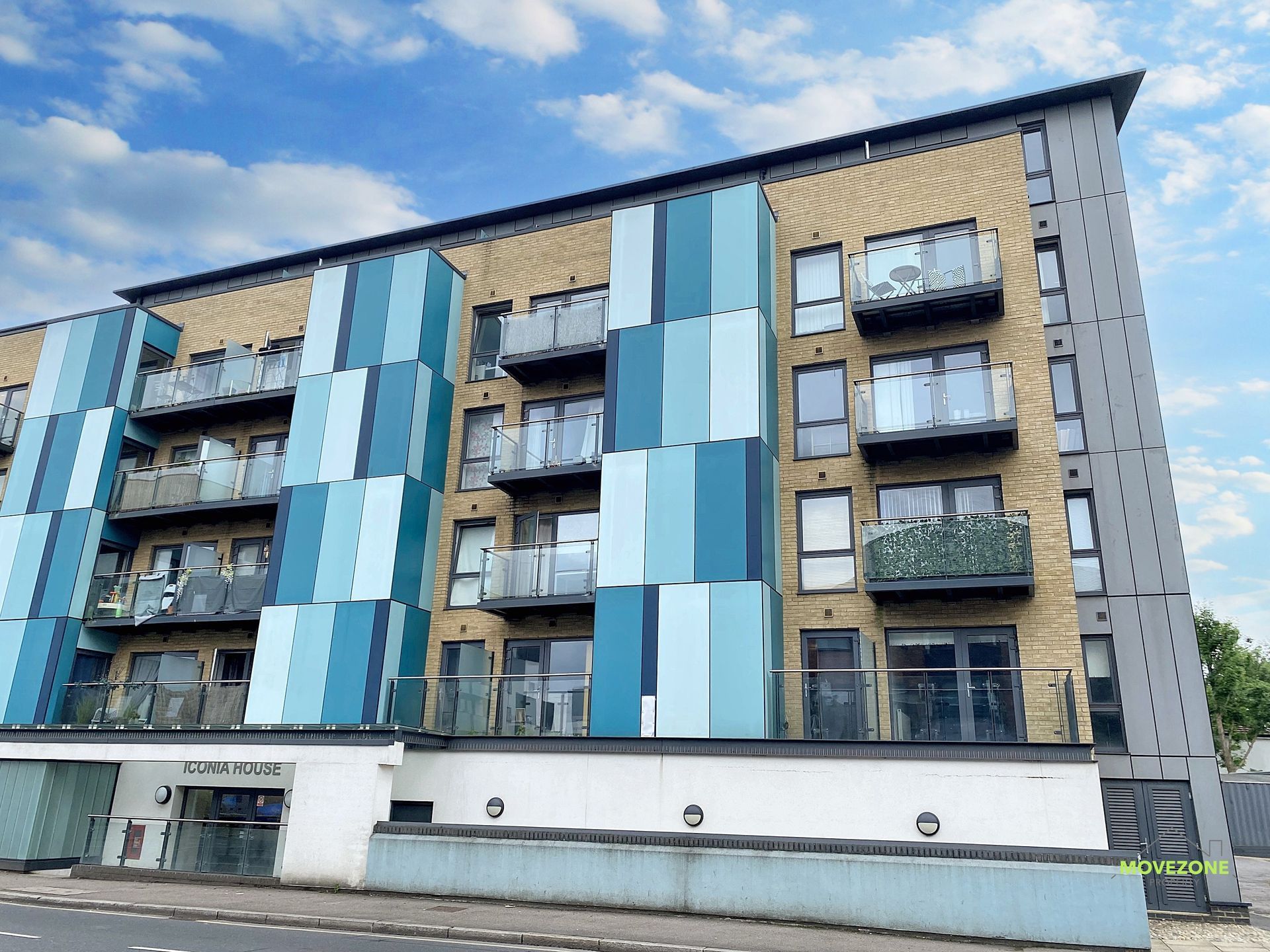 Modern apartment building with blue panels, balconies, and large windows on a street corner