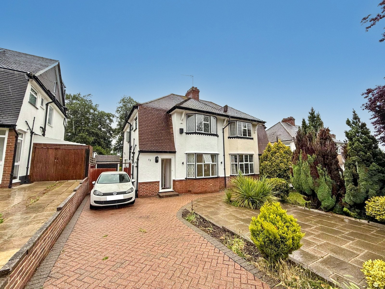 Semi-detached house with brick driveway, white car, and front garden under a clear blue sky