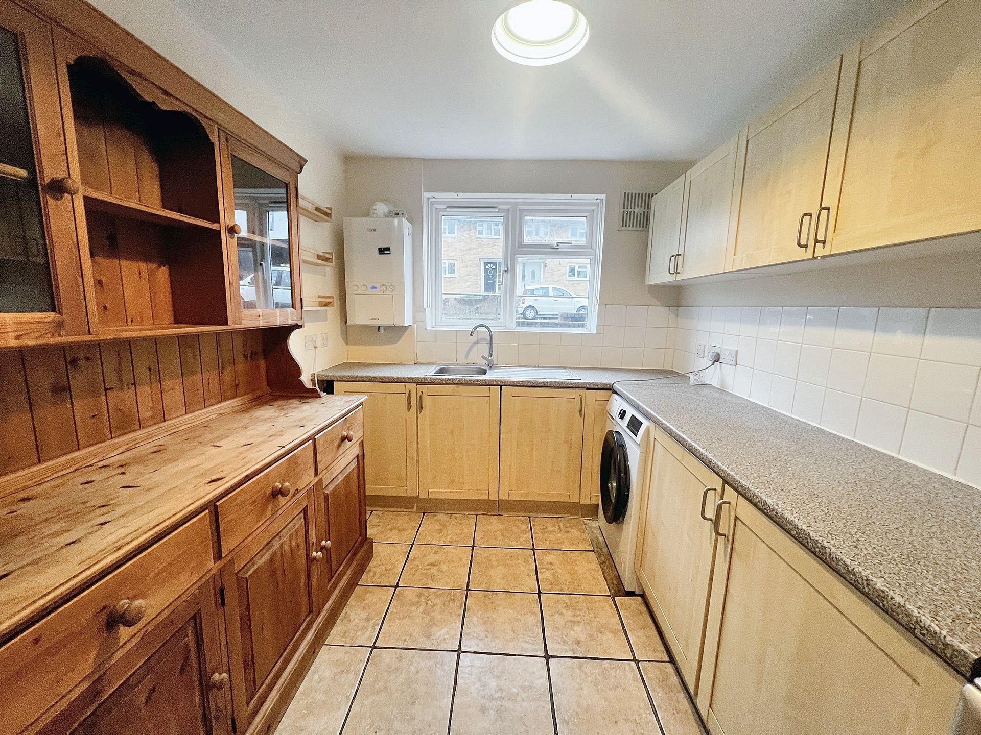 Empty kitchen with wood cabinets, beige counters, tiled floor, and a window over the sink.