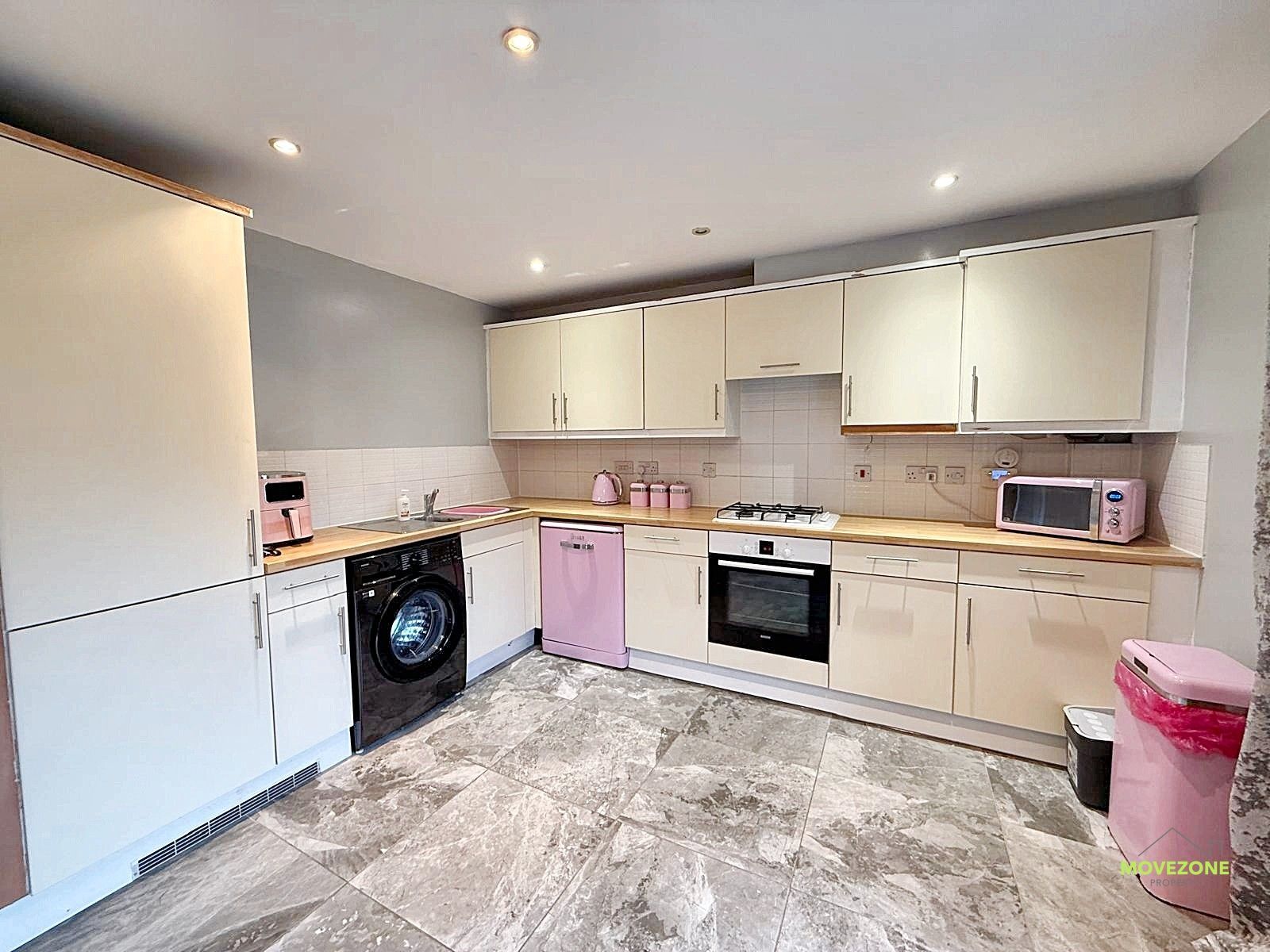 Bright modern kitchen with cream cabinets, pink accents, washing machine, oven, and tiled floor