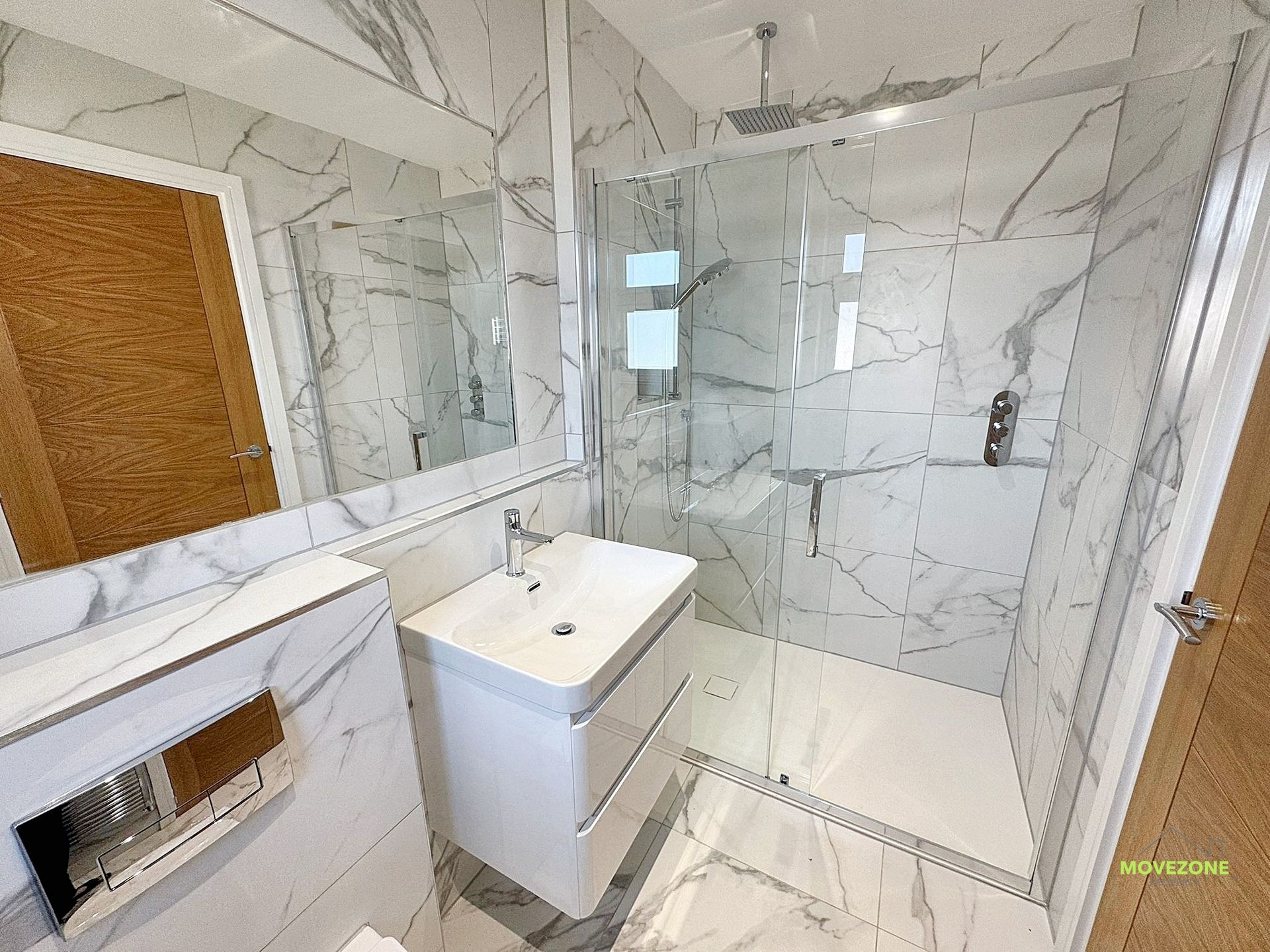 Modern bathroom with marble-look tile, glass shower, floating vanity, and white sink counter