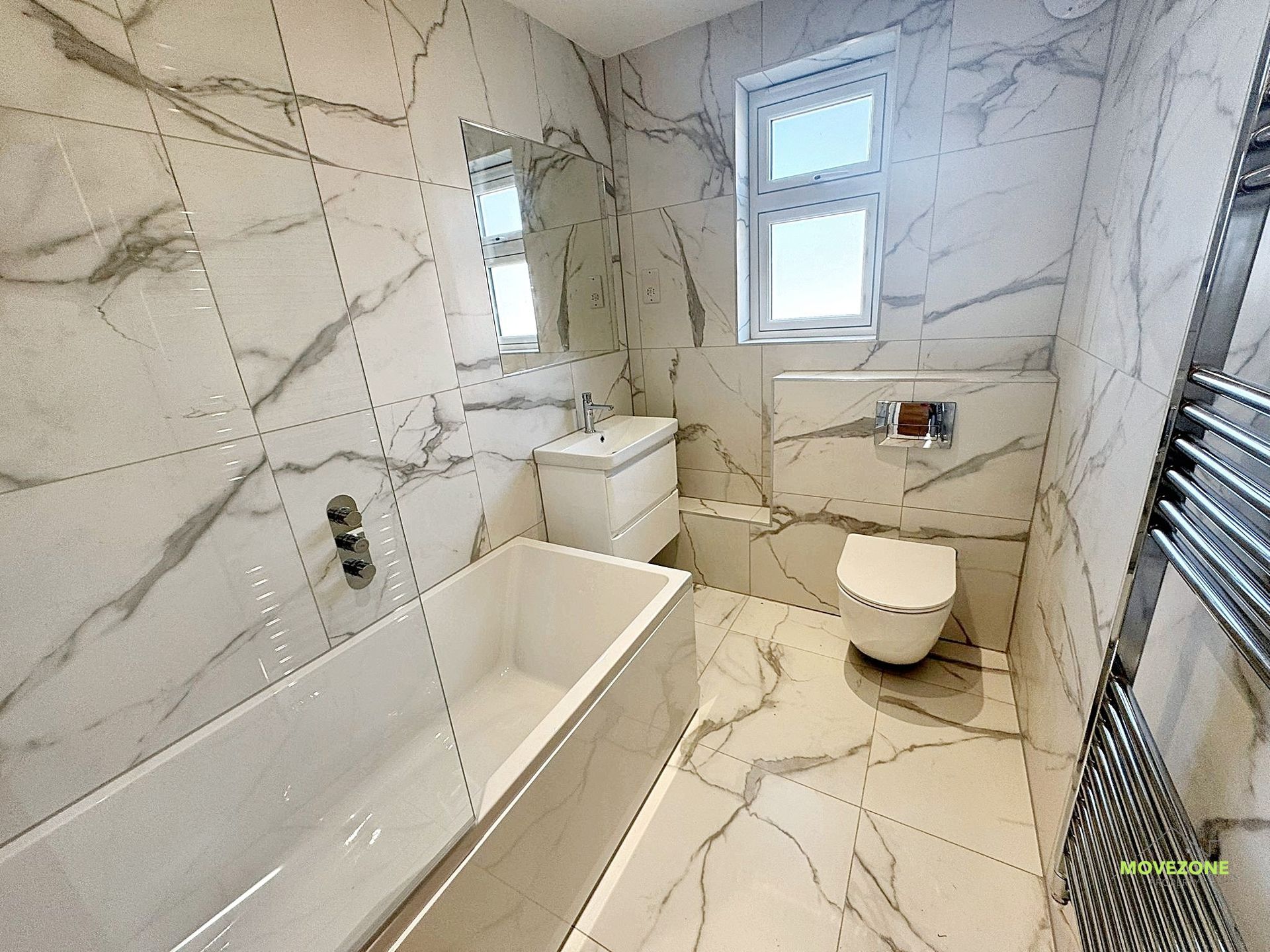Modern marble bathroom with bathtub, toilet, sink, window, and heated towel rail