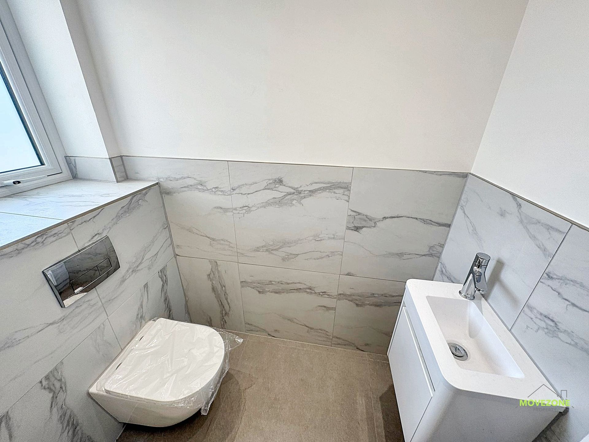 Small modern bathroom with wall-mounted toilet, sink cabinet, and light gray marble tiles.