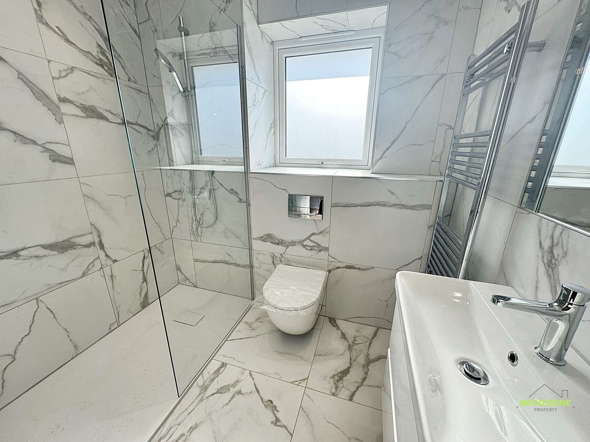 Bright marble-tiled bathroom with toilet, sink, window, and heated towel rack