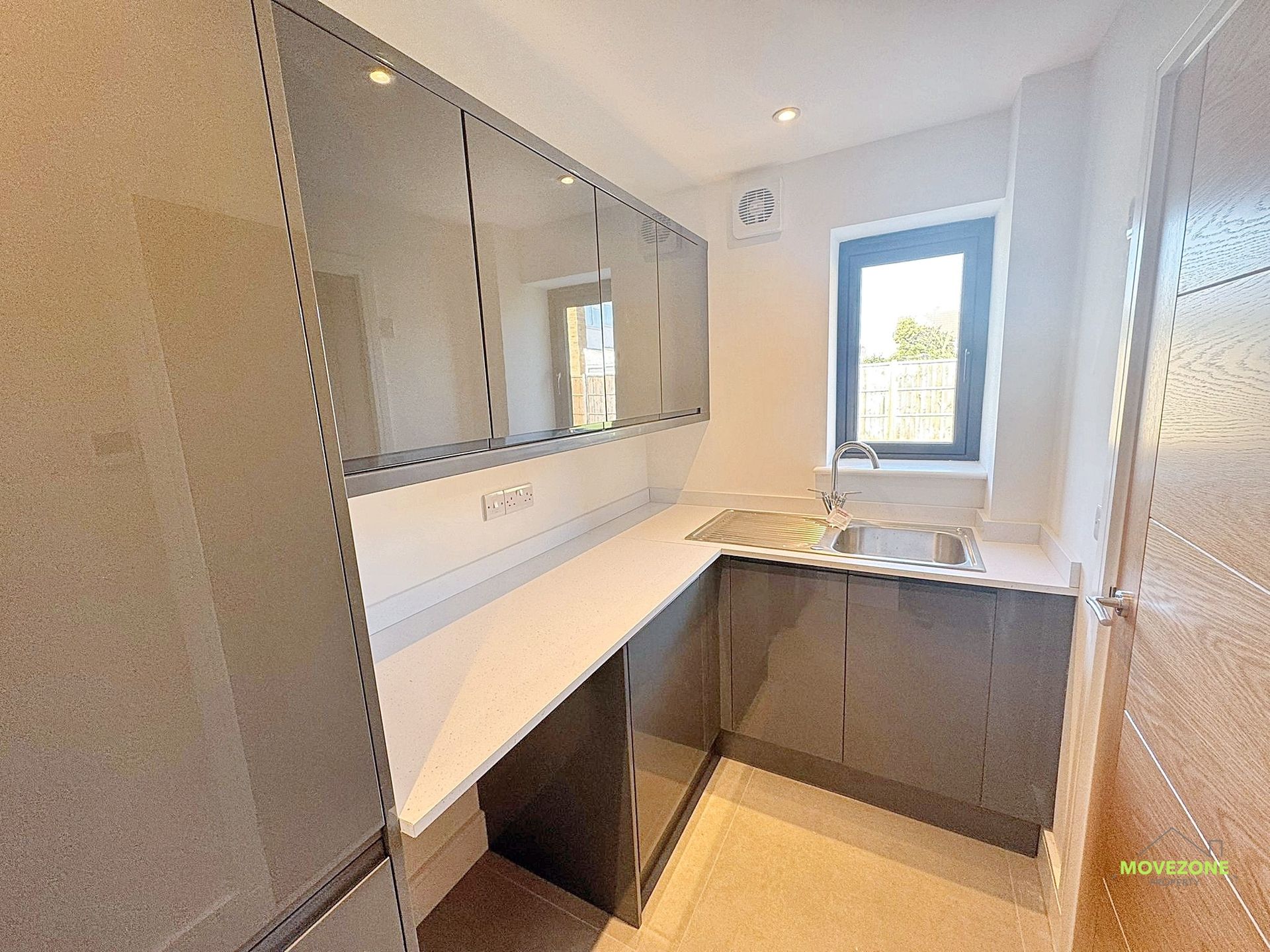 Modern bathroom vanity with gray cabinets, large mirror, white countertop, and a window above the sink.