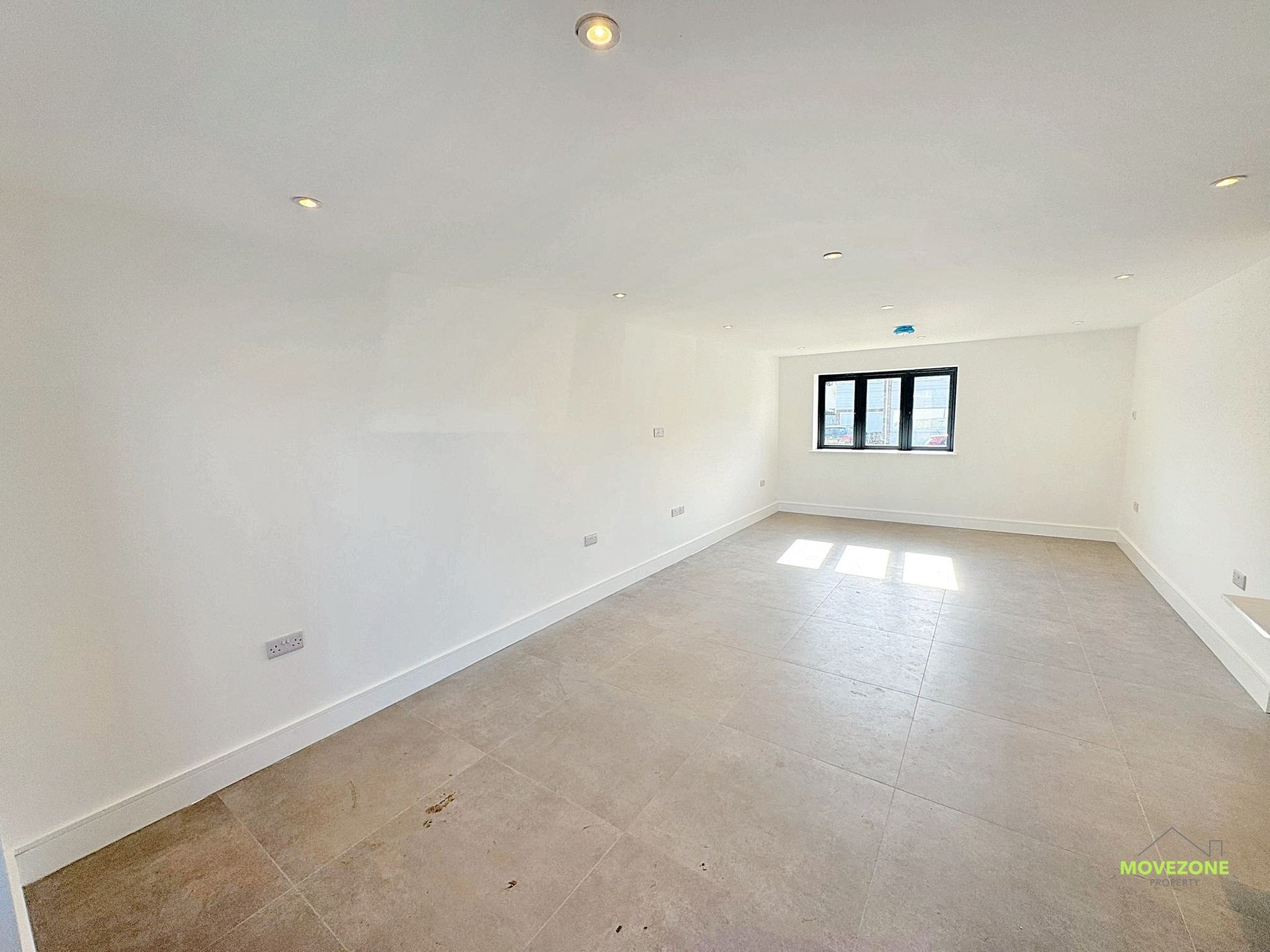 Empty white unfurnished room with tiled floor, recessed lights, and a small window at the far end
