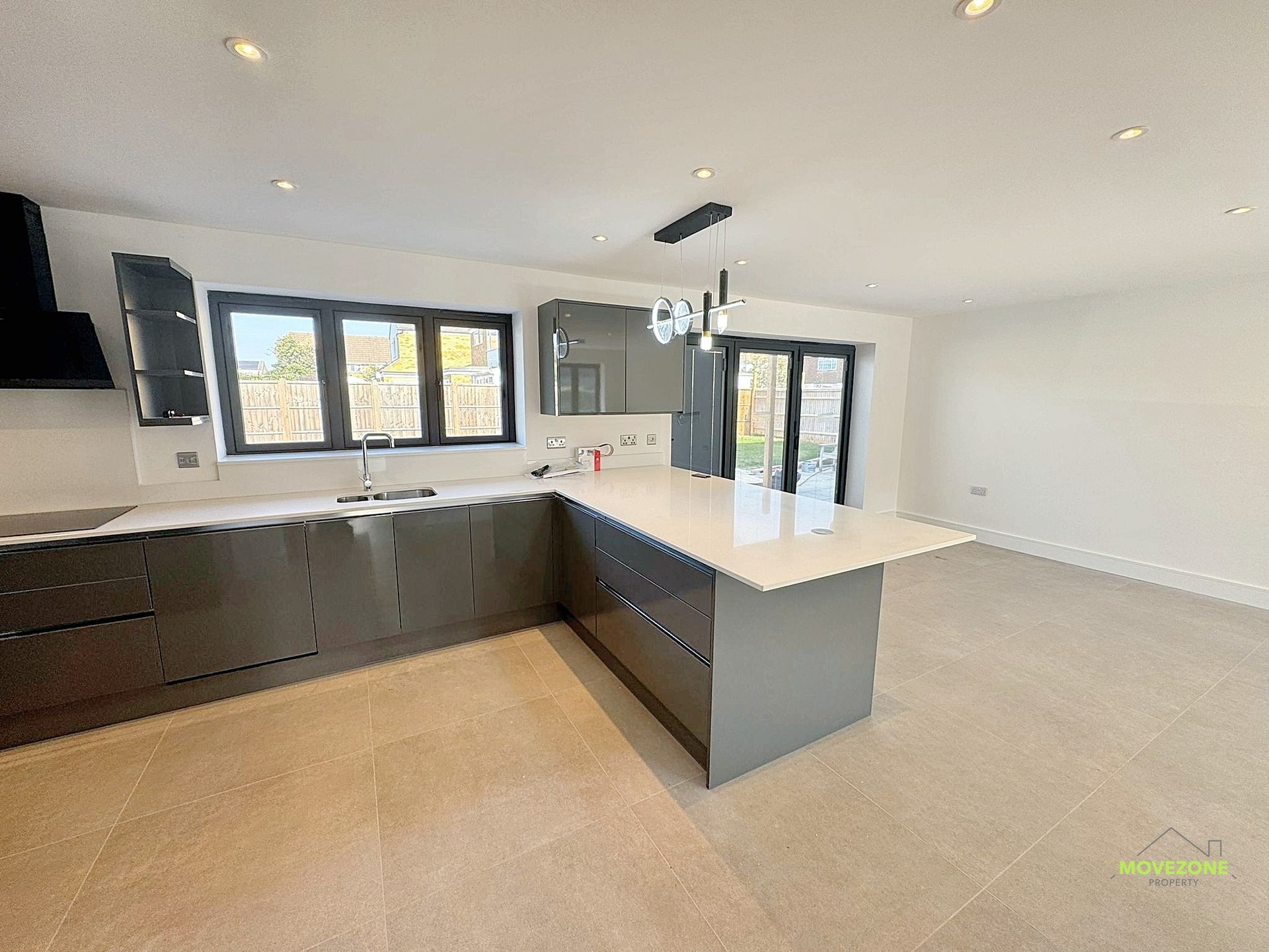 Modern open-plan kitchen with dark cabinets, white island, and large windows in a bright living space