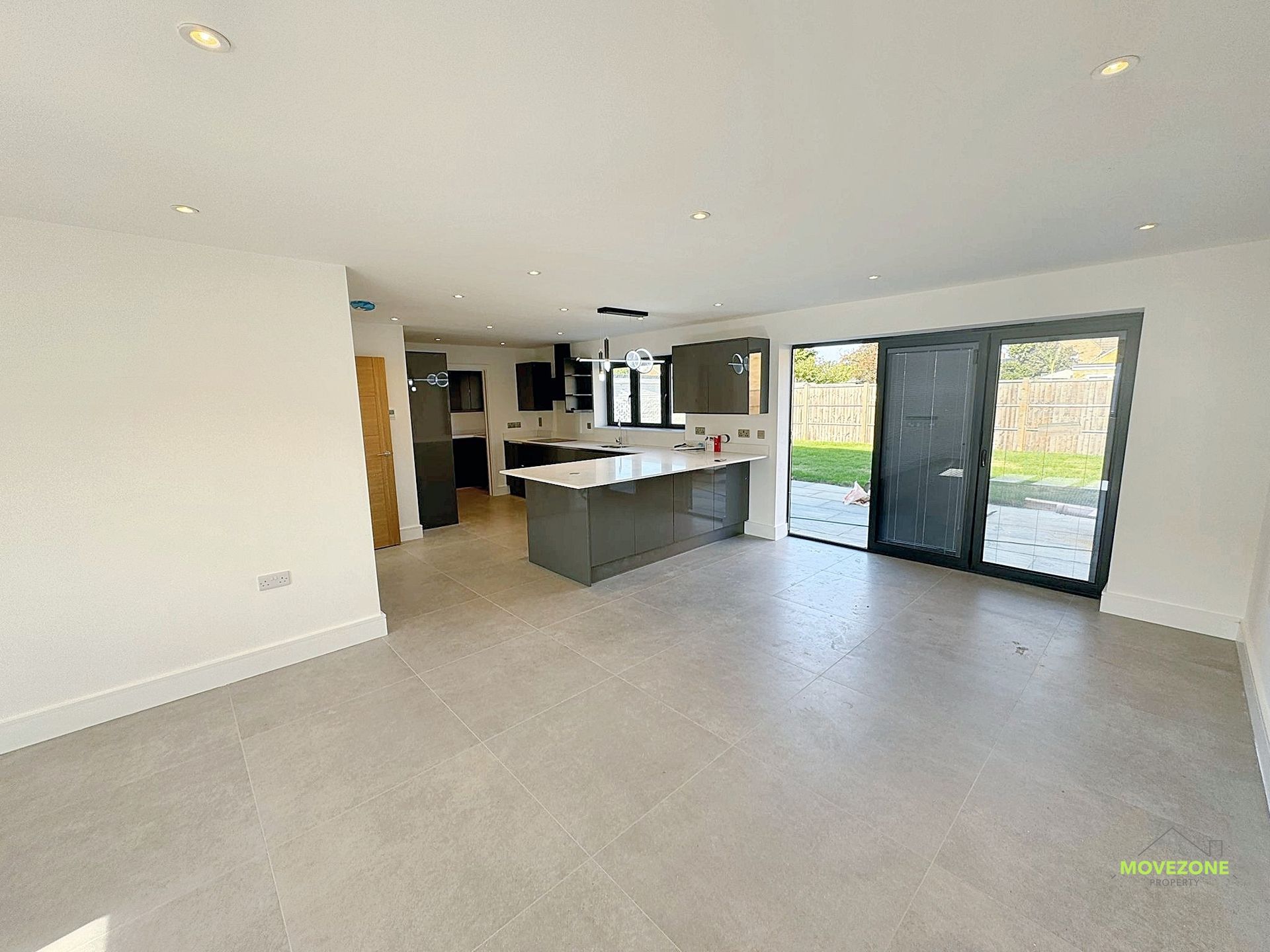 Bright open-plan living room with light tile floors, kitchen island, and glass doors to a patio.