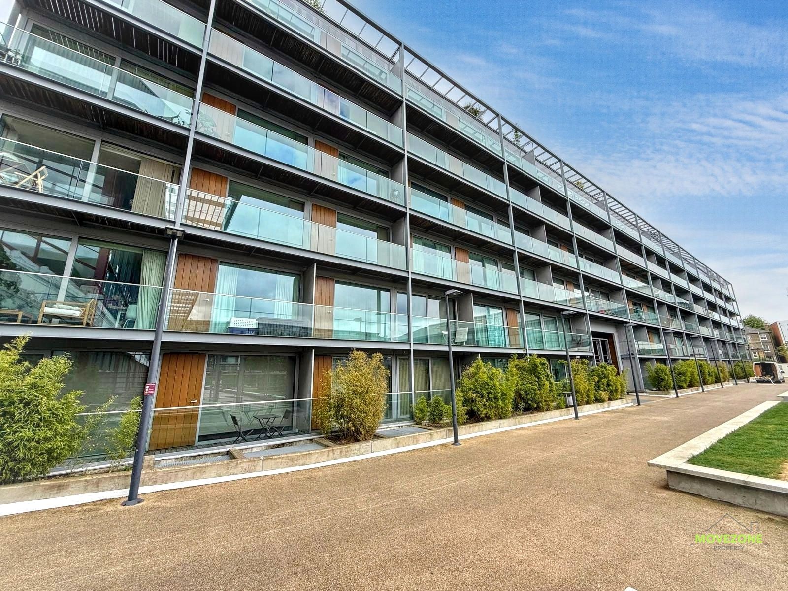 Modern apartment building with glass balconies and a landscaped walkway under a blue sky