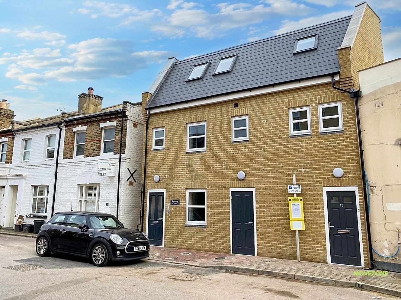 Row of brick townhouses with a black car parked on a cobblestone street