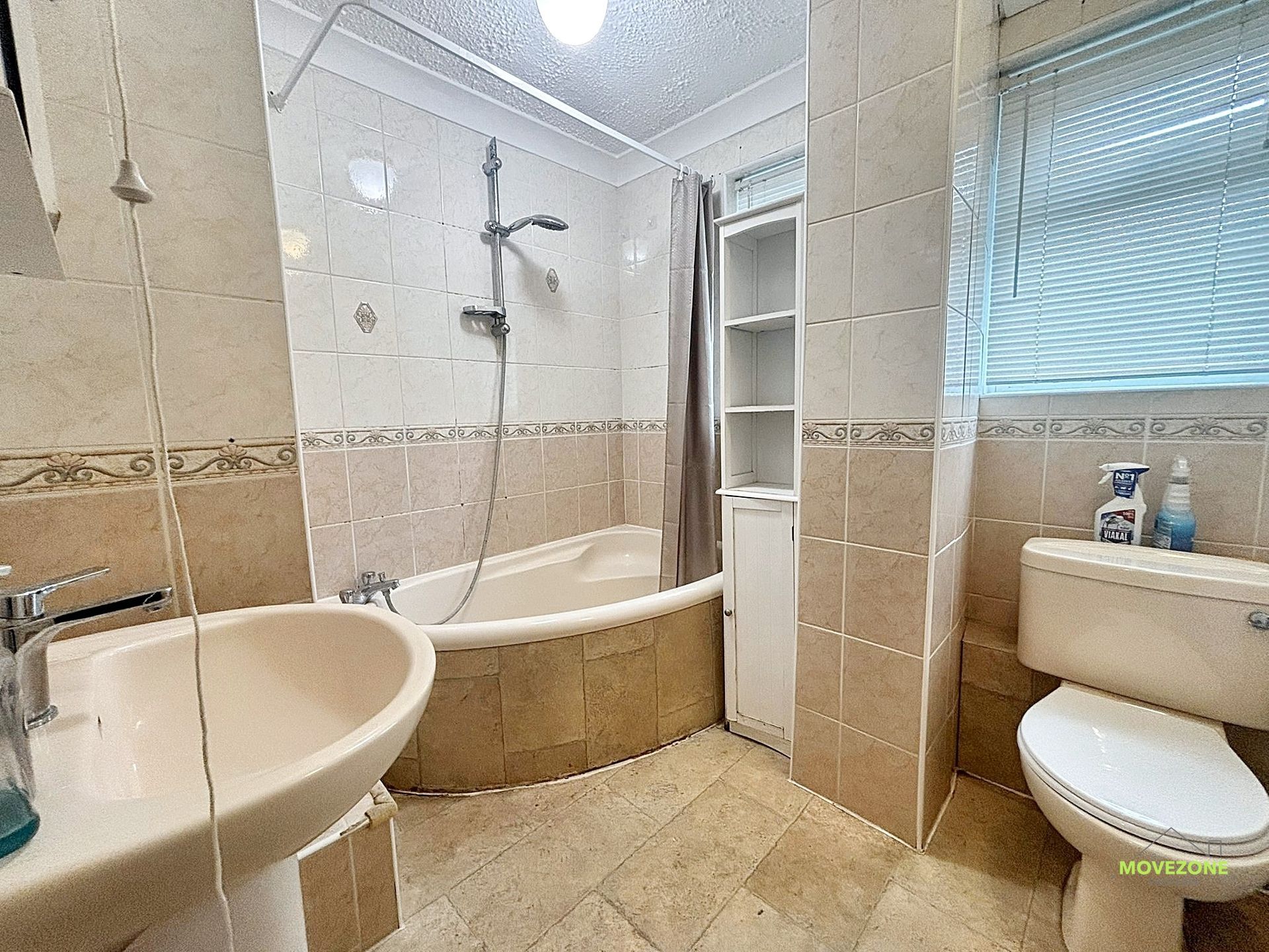Small beige tiled bathroom with a bathtub, sink, toilet, and walk-in shower.
