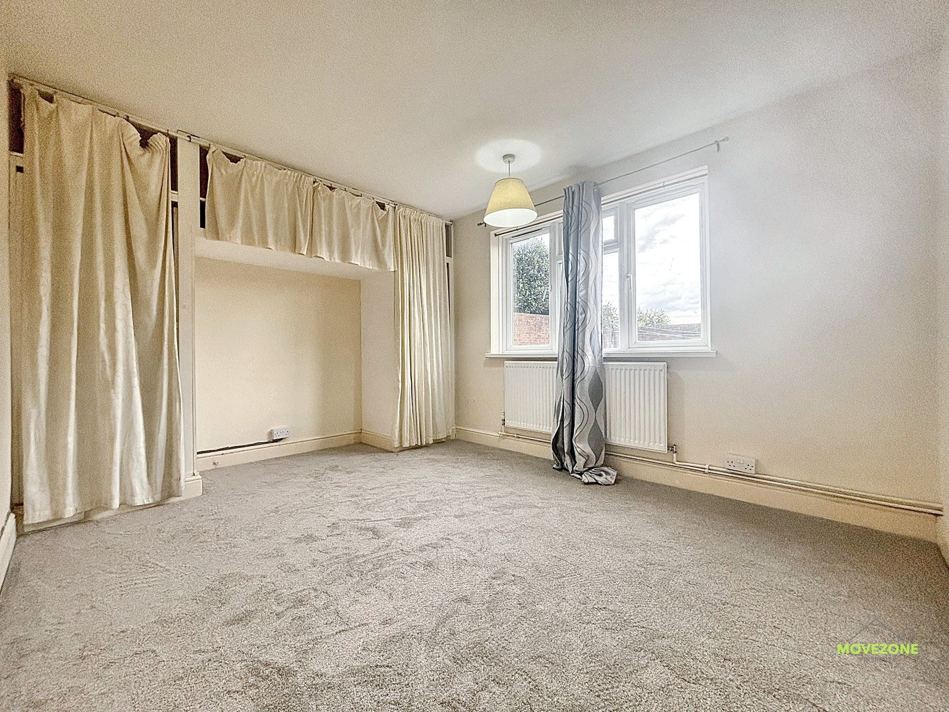 Empty beige carpeted living room with curtains, large windows, and a ceiling light