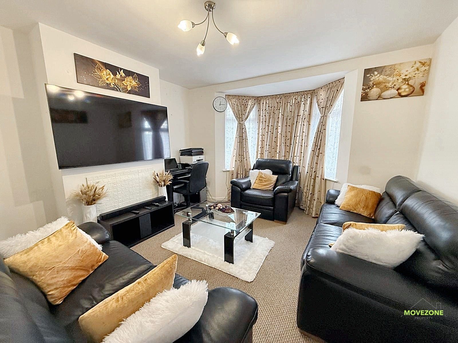 Bright living room with black sofas, beige curtains, a wall TV, and a glass coffee table
