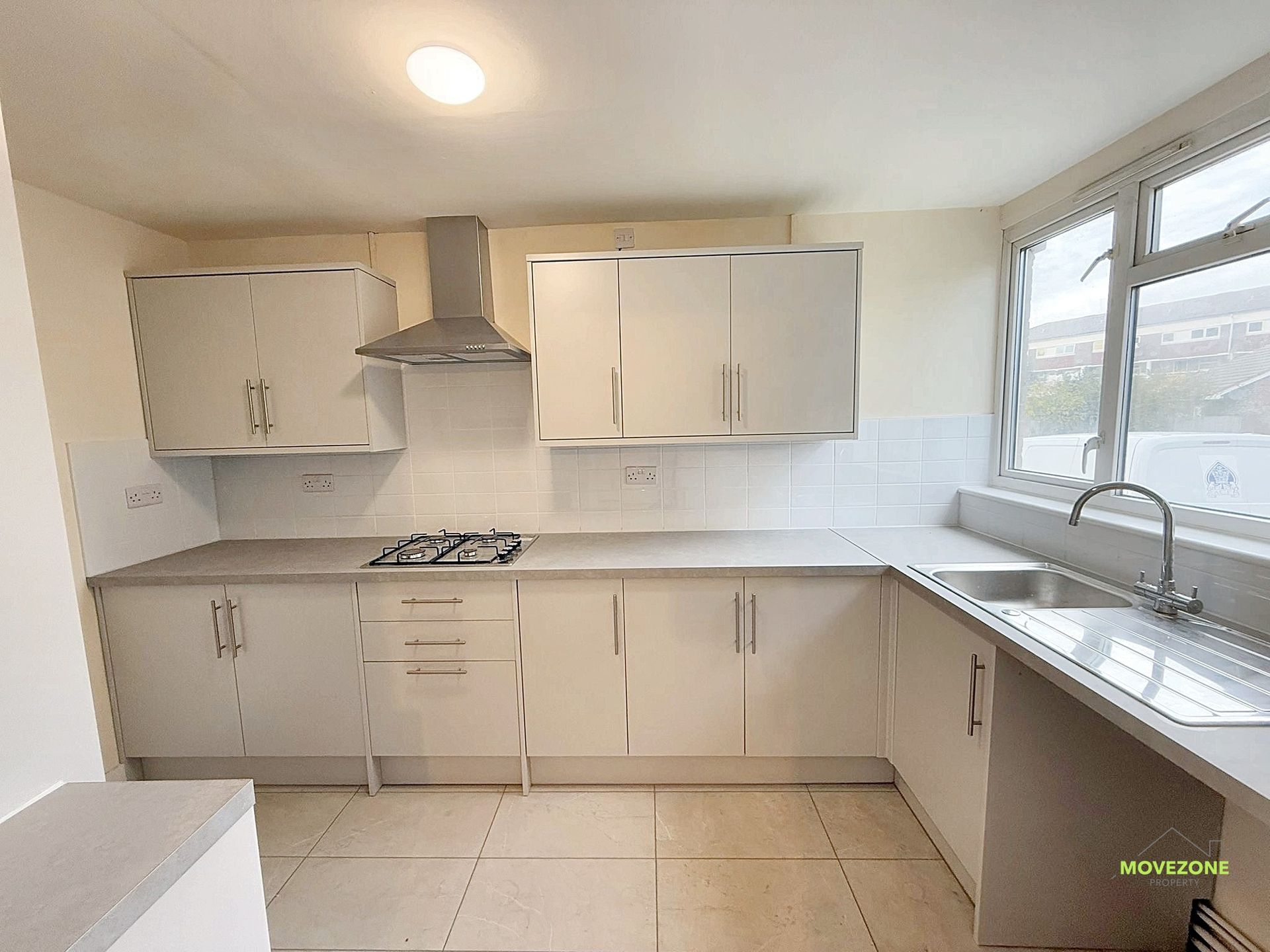 Bright, modern white kitchen with cabinets, tiled floor, gas stove, and a large window over the sink.