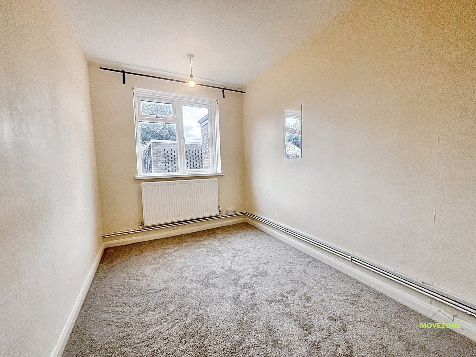 Empty beige carpeted room with a window, radiator, and ceiling light.