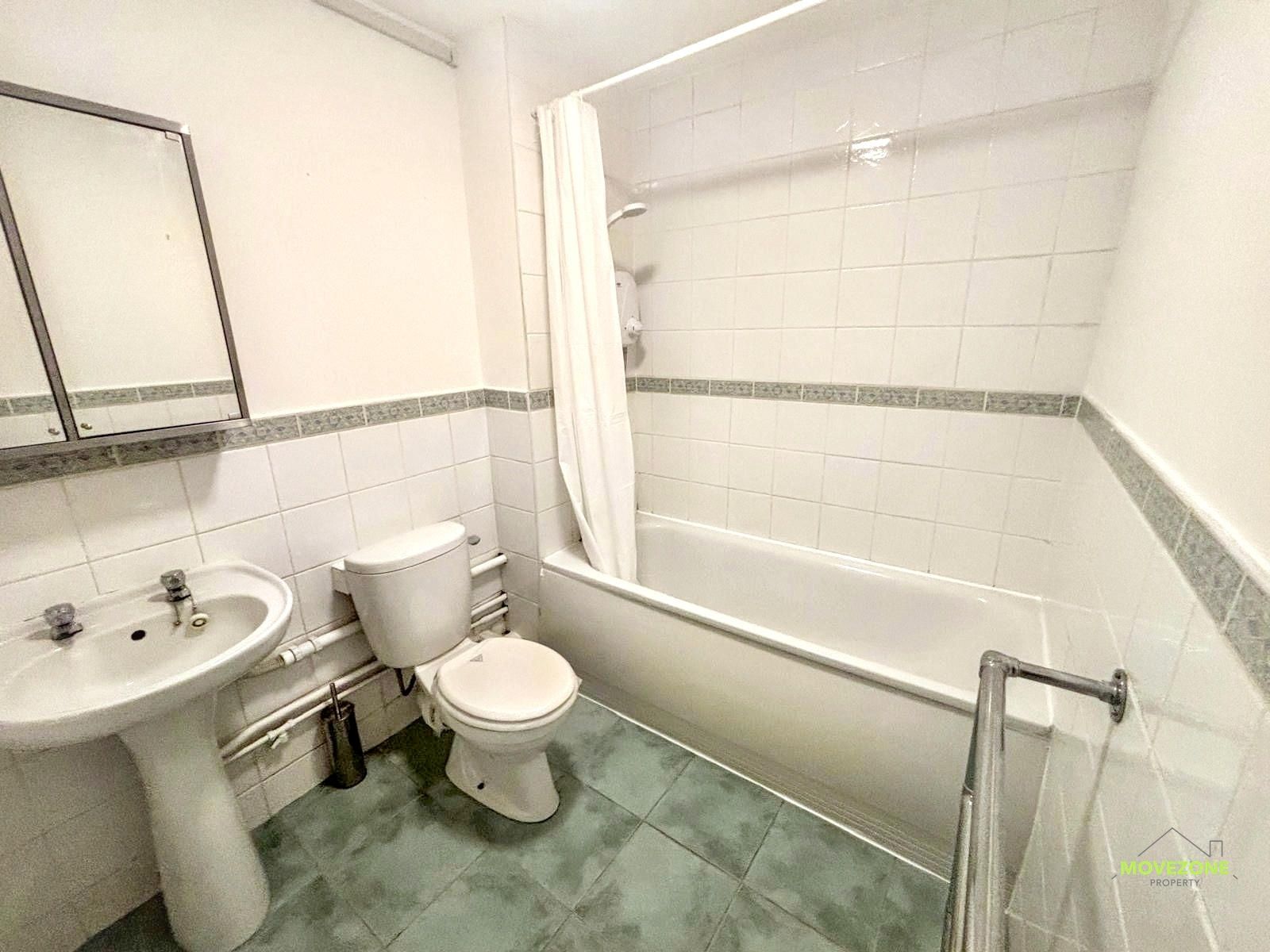 Small white bathroom with sink, toilet, bathtub, green floor, and mirror.