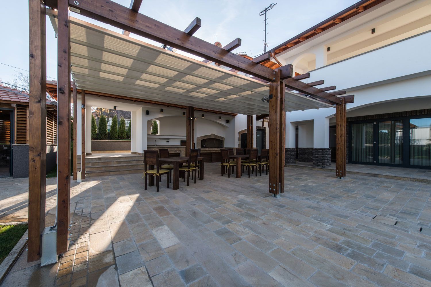 Outdoor patio with pergola, dining table, and stone paving beside a modern house