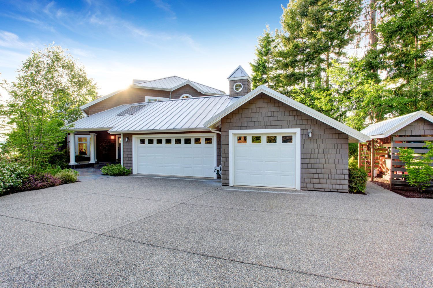 Modern house exterior with double garage, stone siding, and a large paved driveway surrounded by trees.