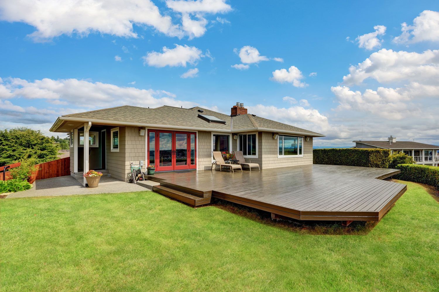 Modern single-story house with a large wooden deck and green lawn under a blue sky