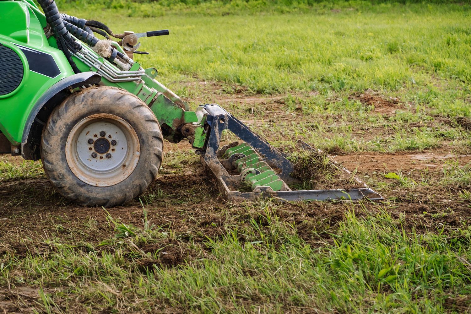 Green tractor tilling muddy soil in a grassy field