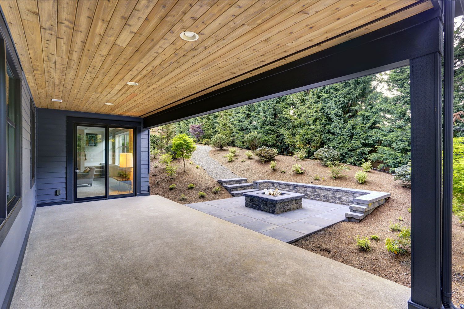 Covered patio with wood ceiling, concrete floor, and a fire pit overlooking a landscaped yard