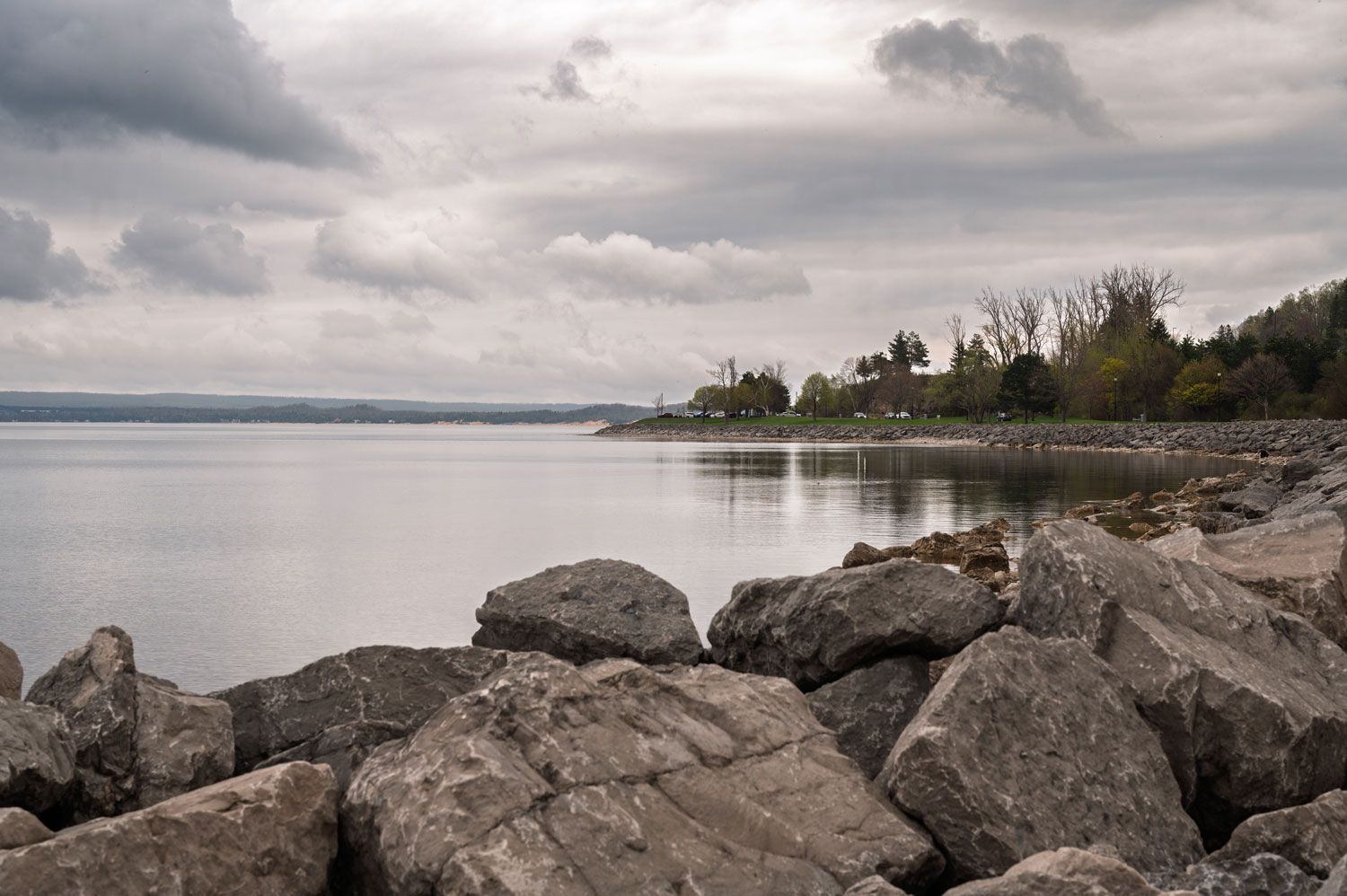 Rocky shoreline beside a calm lake under a cloudy gray sky