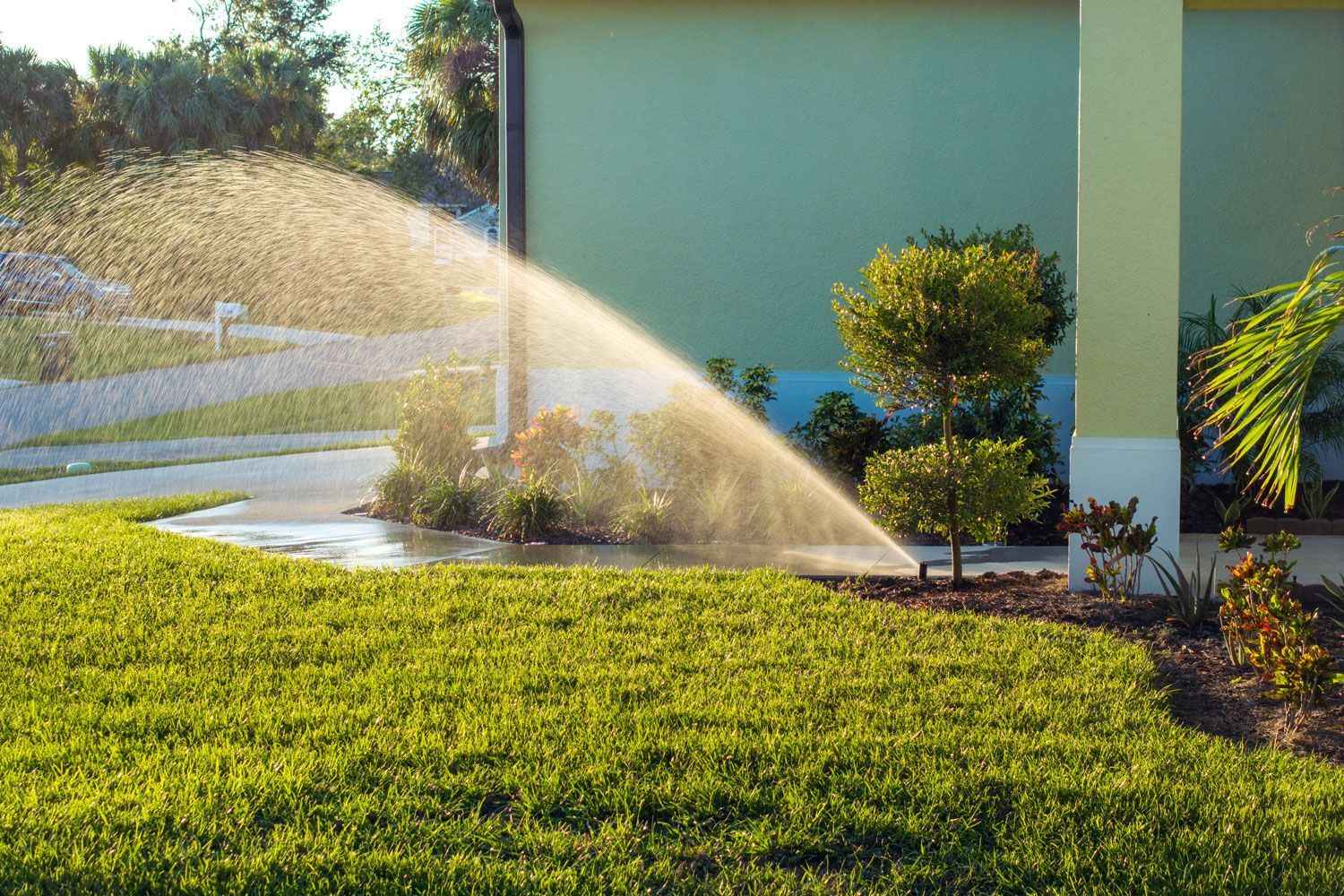 Sprinkler watering a green lawn beside a house in bright sunlight