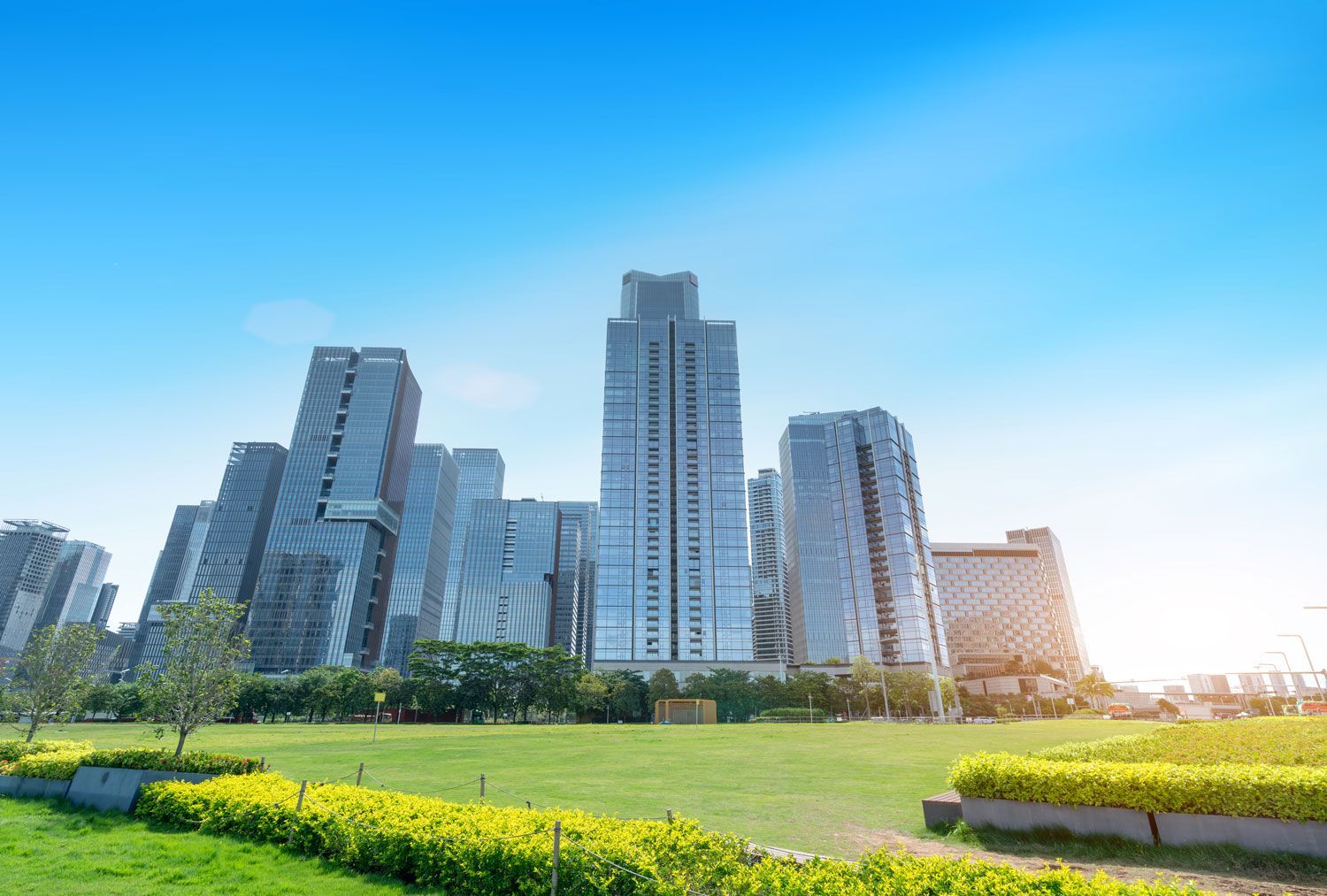 Modern city skyline with tall high-rises beside a green park under a bright blue sky