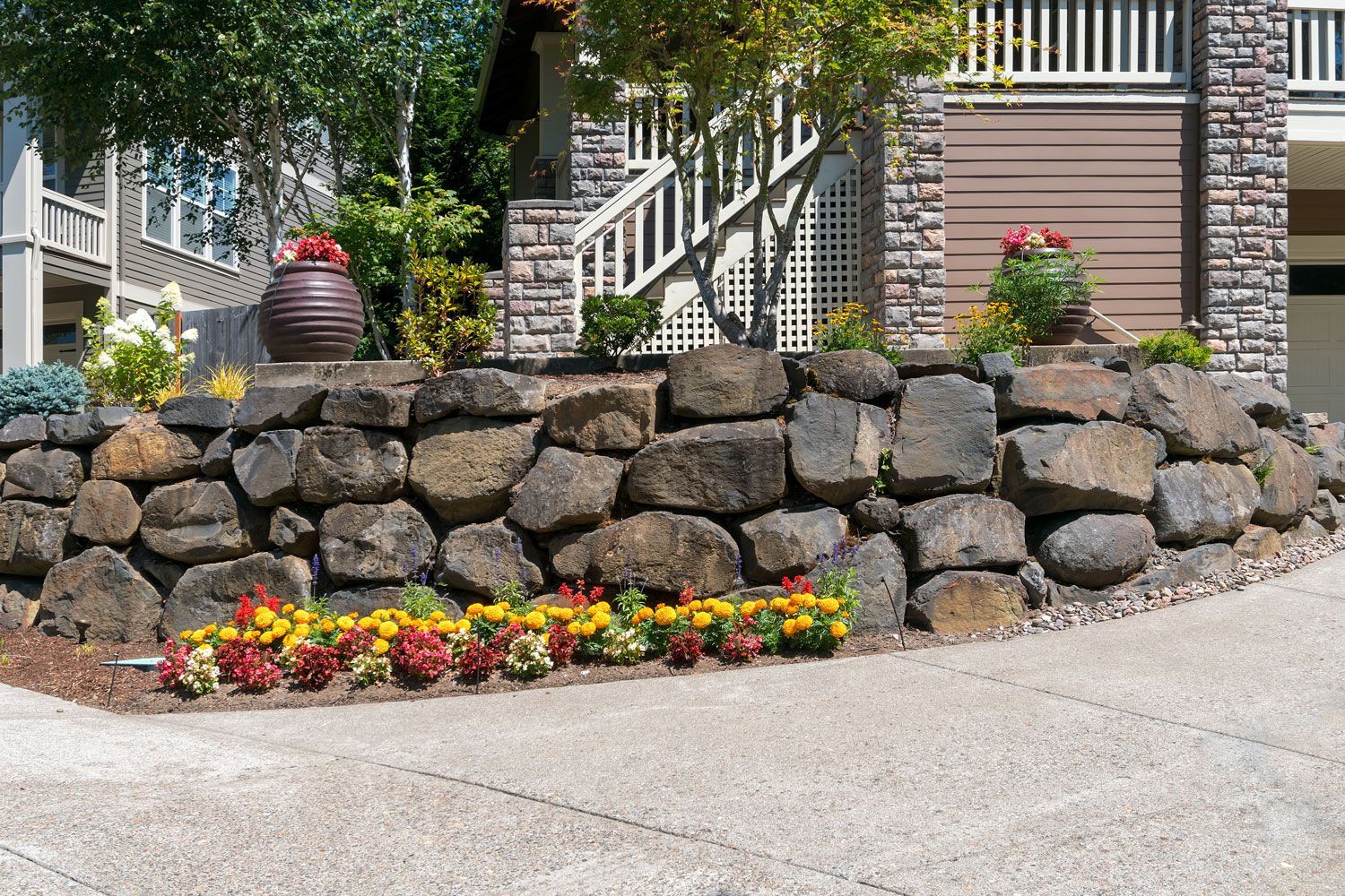 Stone retaining wall with red flowers and potted plants beside a house entrance